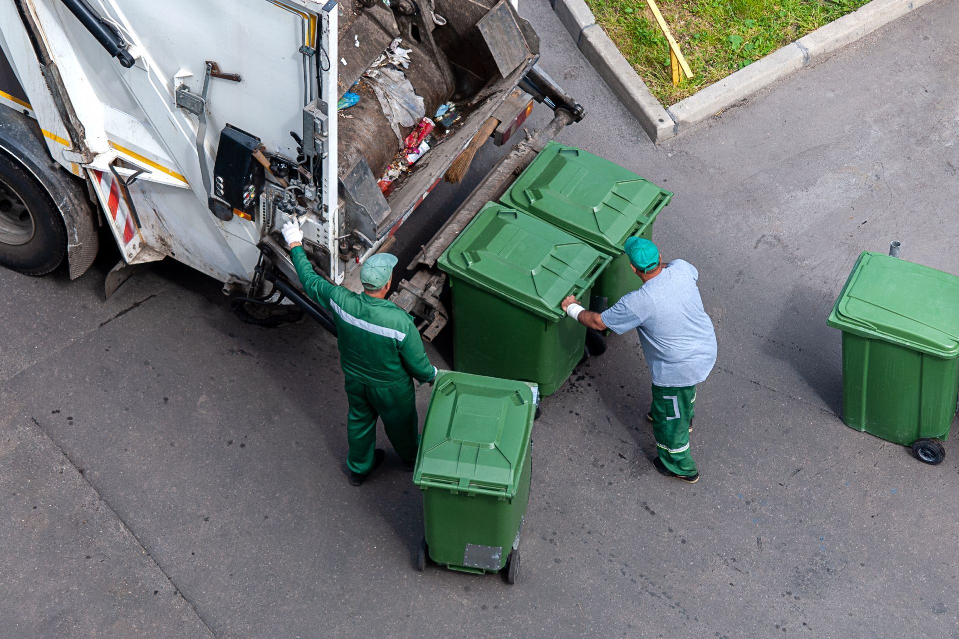 Garbage truck loading green bins, workers in green and blue uniforms on a street.