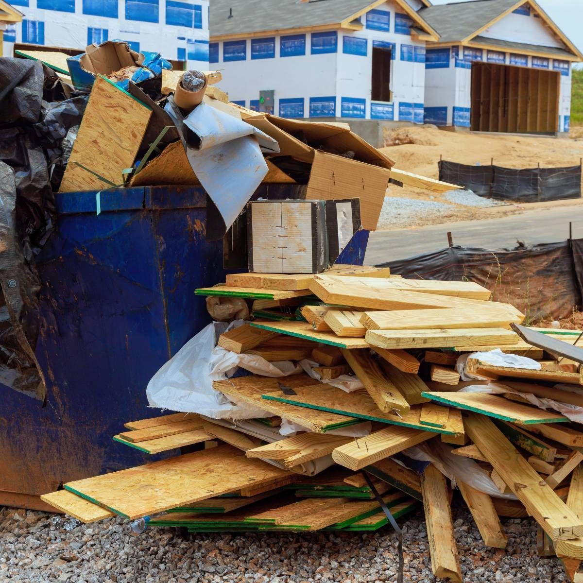Construction debris, including wood and other materials, overflowing a blue dumpster at a construction site.