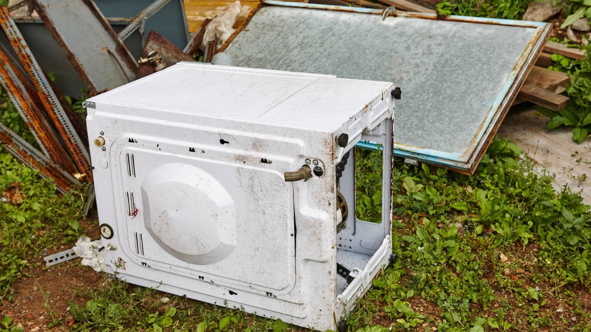 Garbage truck worker in green overalls operates machinery against a blue sky backdrop.