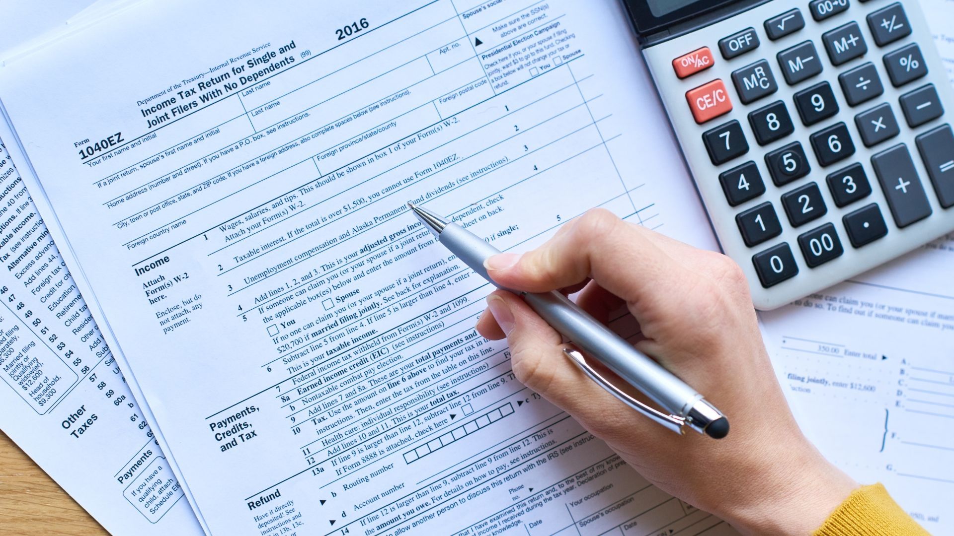 A person is writing on a piece of paper next to a calculator.