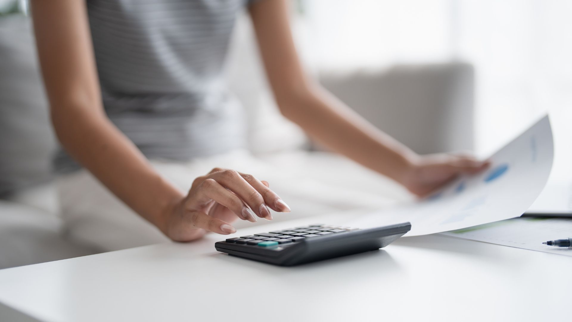 A woman is using a calculator while holding a piece of paper.