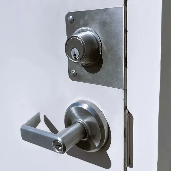 Close-up View Of A Commercial Door Lever And Deadbolt With A Door Reinforcement Plate. Close-up View Of A Commercial Door Lever And Deadbolt With A Door Reinforcement Plate.