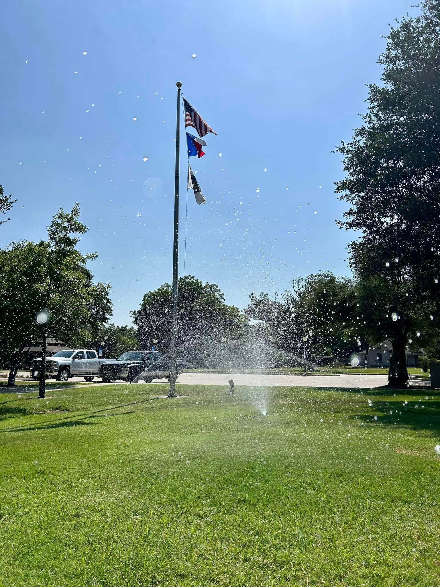 A Sprinkler Is Spraying Water in A Park with A Flag in The Background - Collinsville, TX - L5 Irrigation