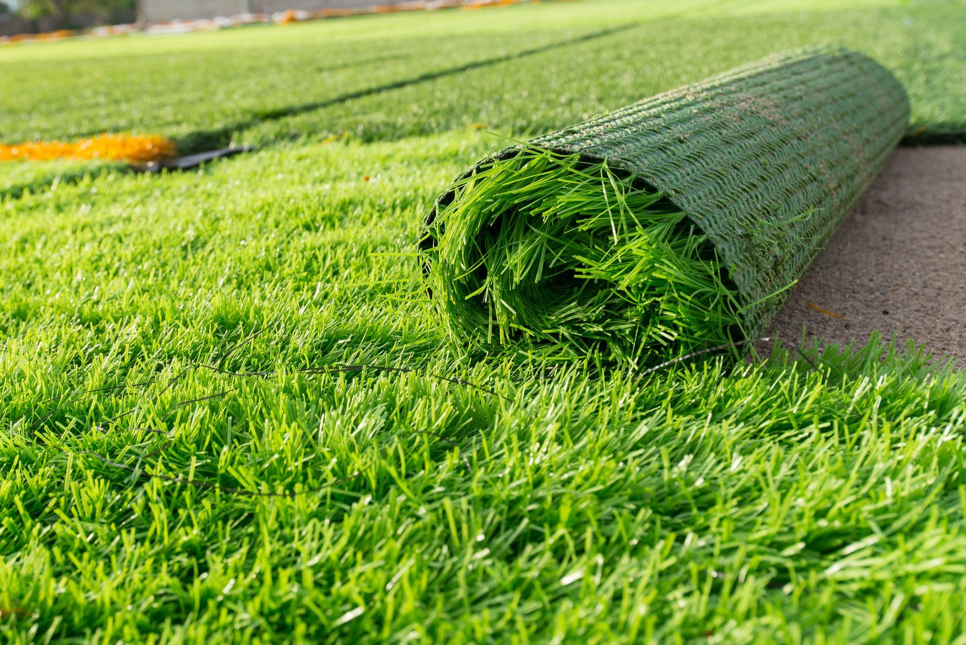 A roll of bright green artificial turf being unrolled onto a grassy area.