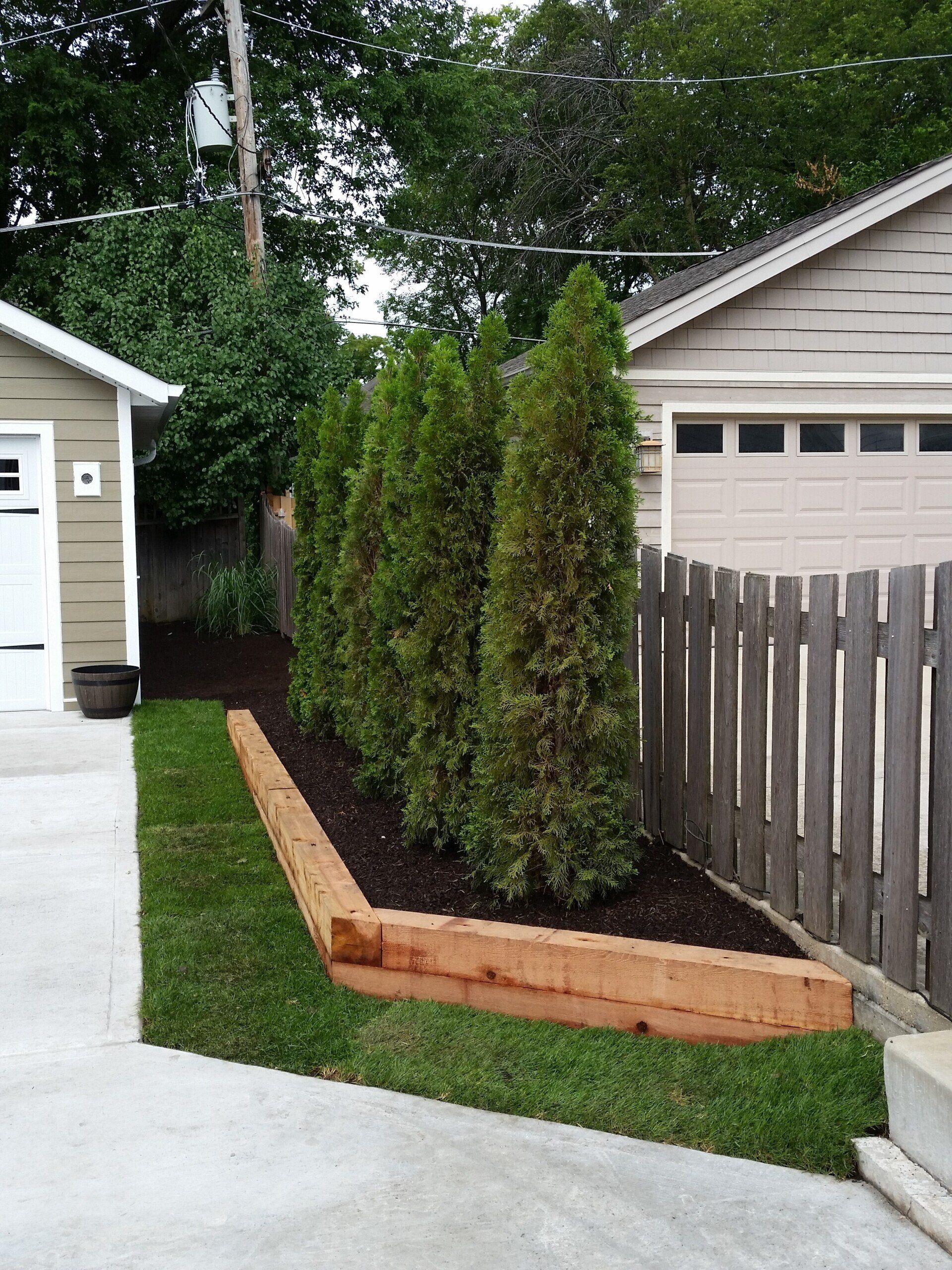 A wooden fence surrounds a yard with trees and a garage in the background
