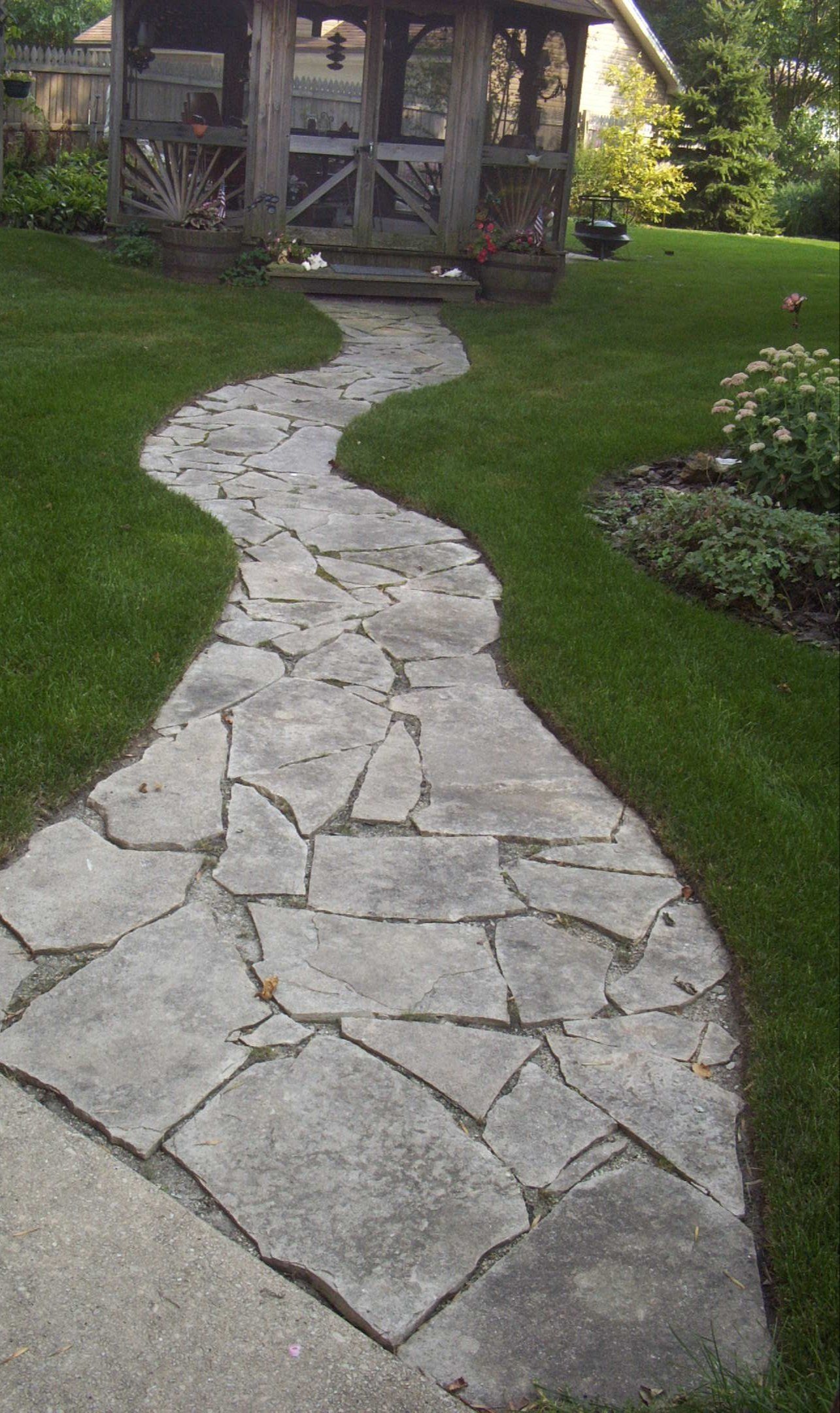 A stone walkway leading to a gazebo in a backyard.