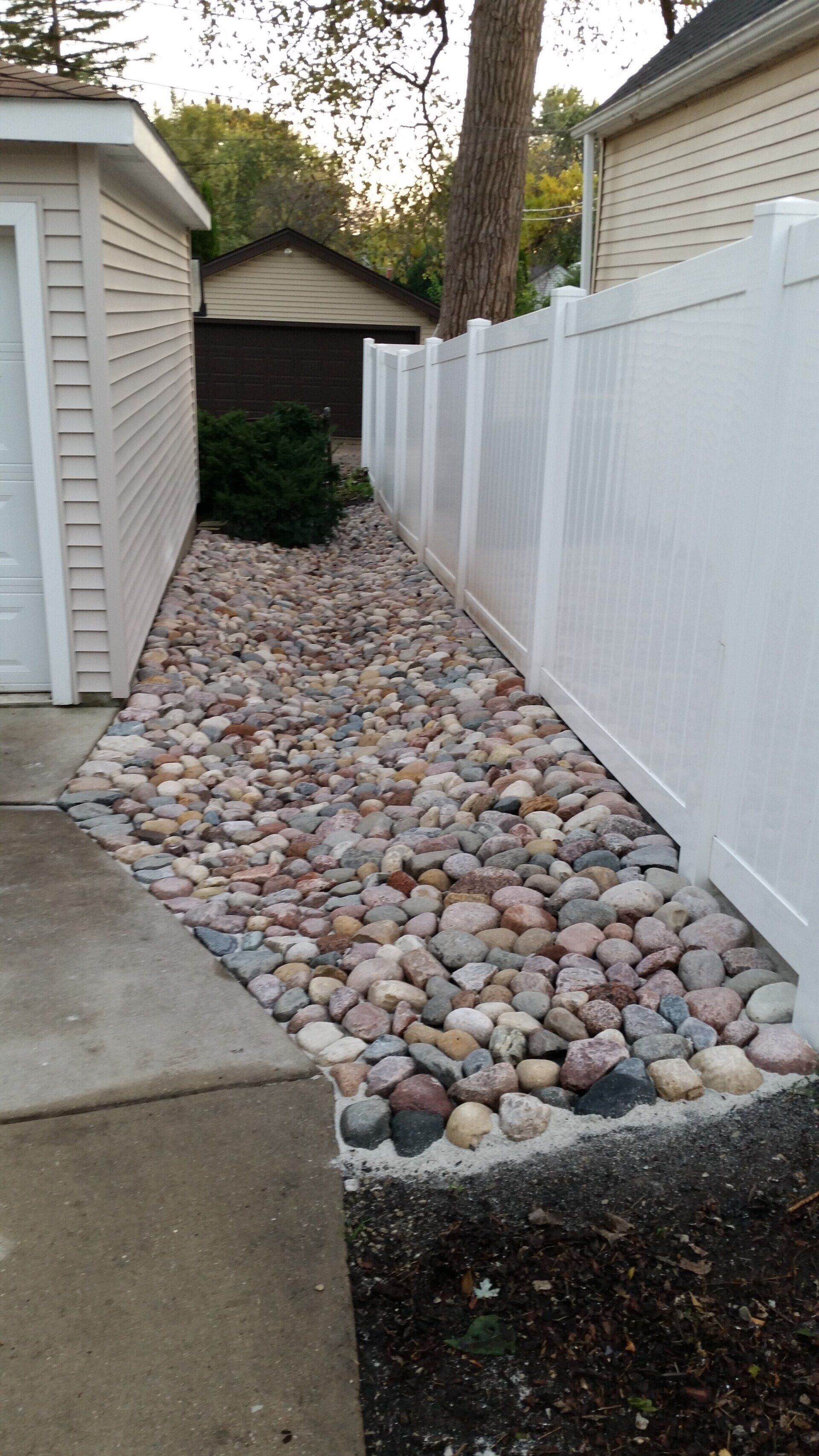 A white fence surrounded by rocks next to a garage.