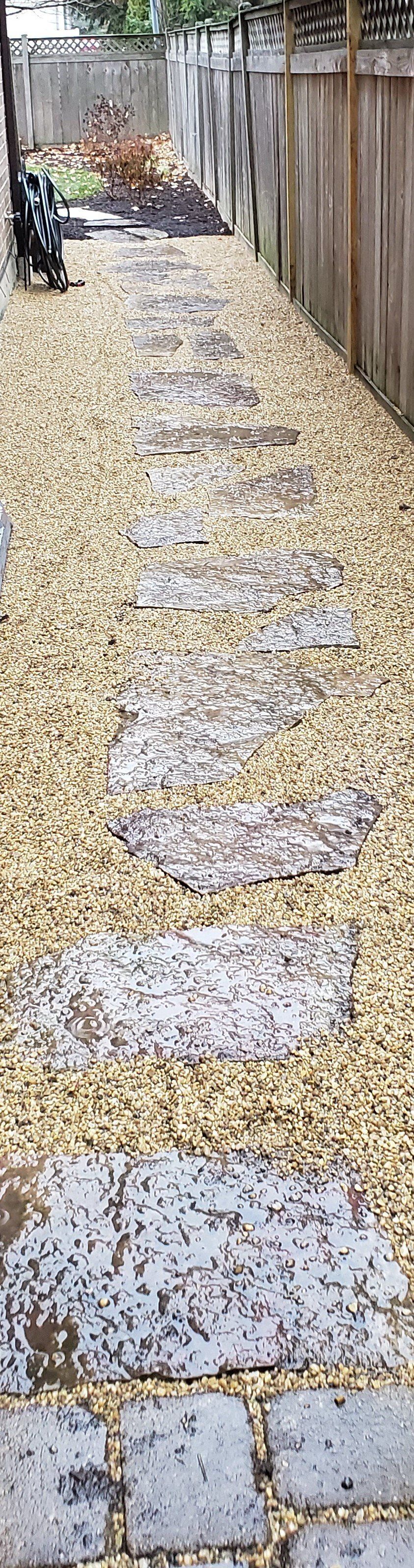 A stone walkway leading to a fence with a bench in the background.
