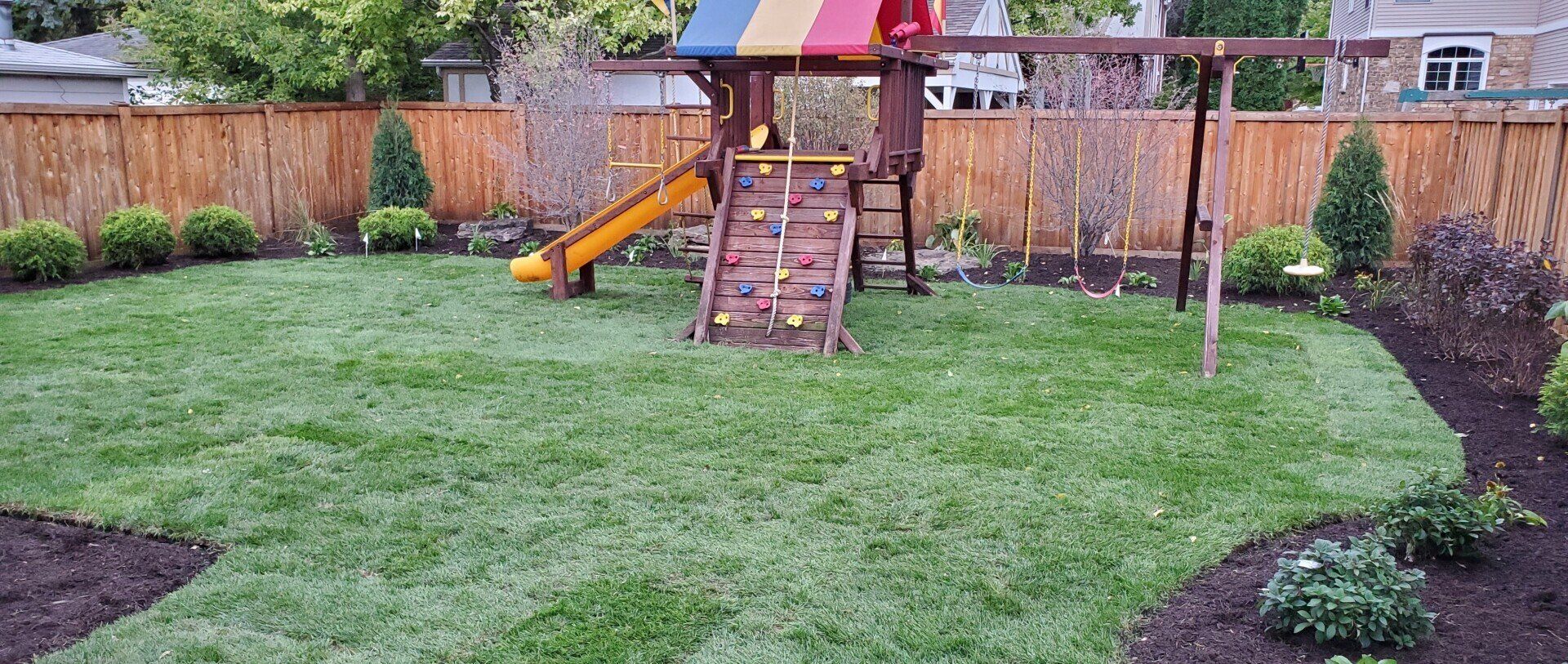 A backyard with a playground and a wooden fence.