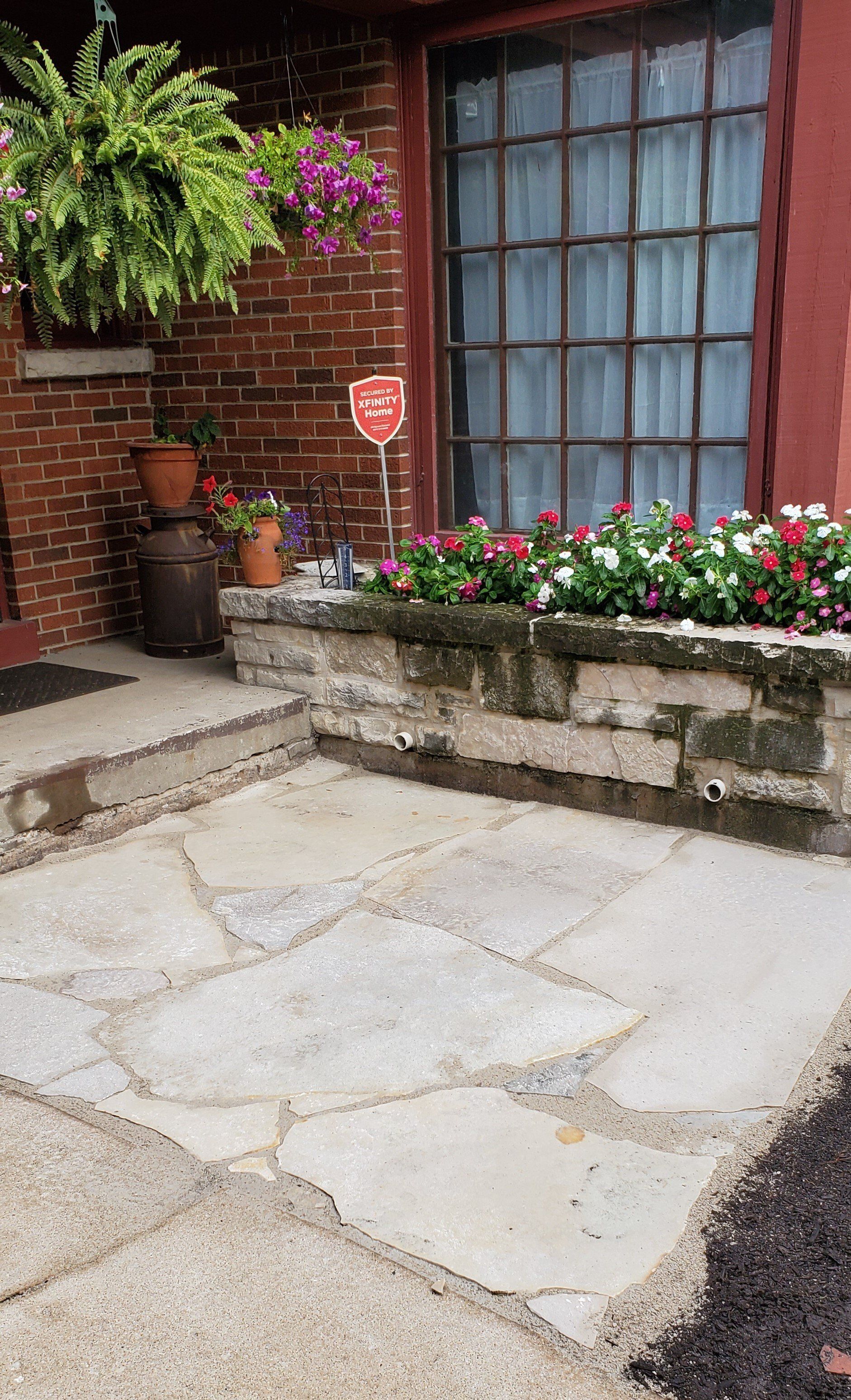 A stone patio with flowers in front of a brick building.
