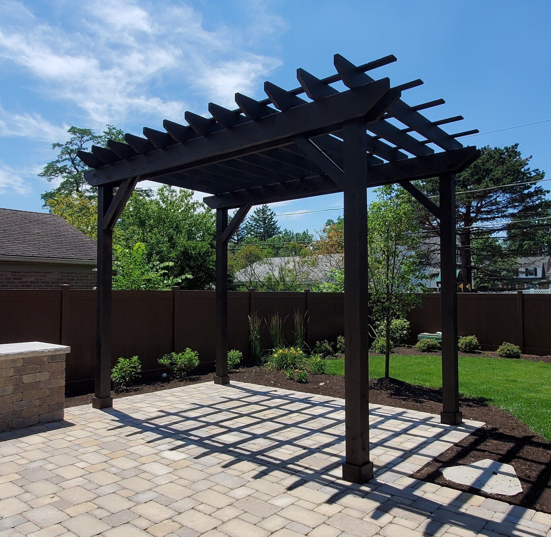A pergola is sitting on a brick patio in a backyard