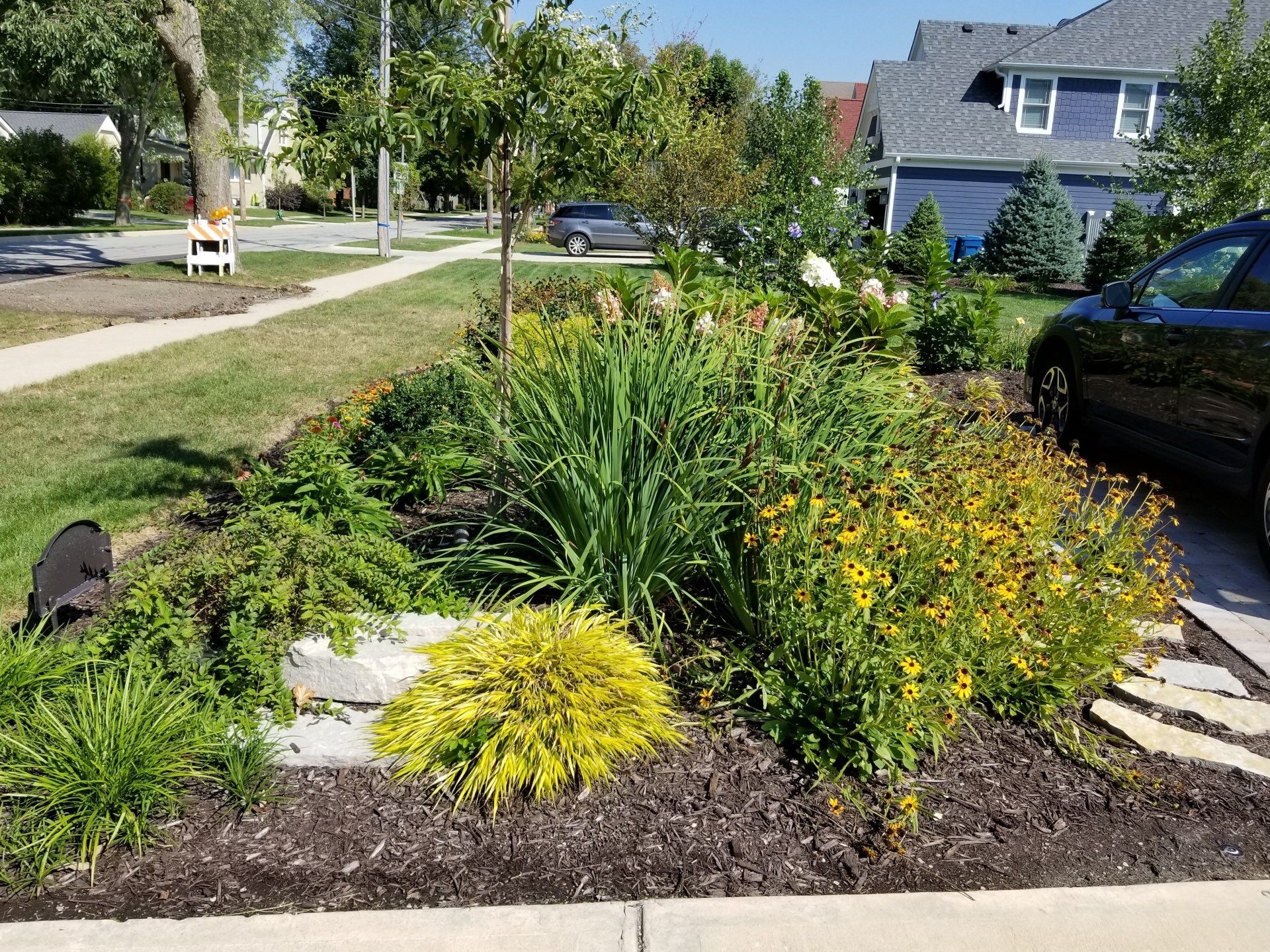 A black car is parked in a driveway next to a garden.