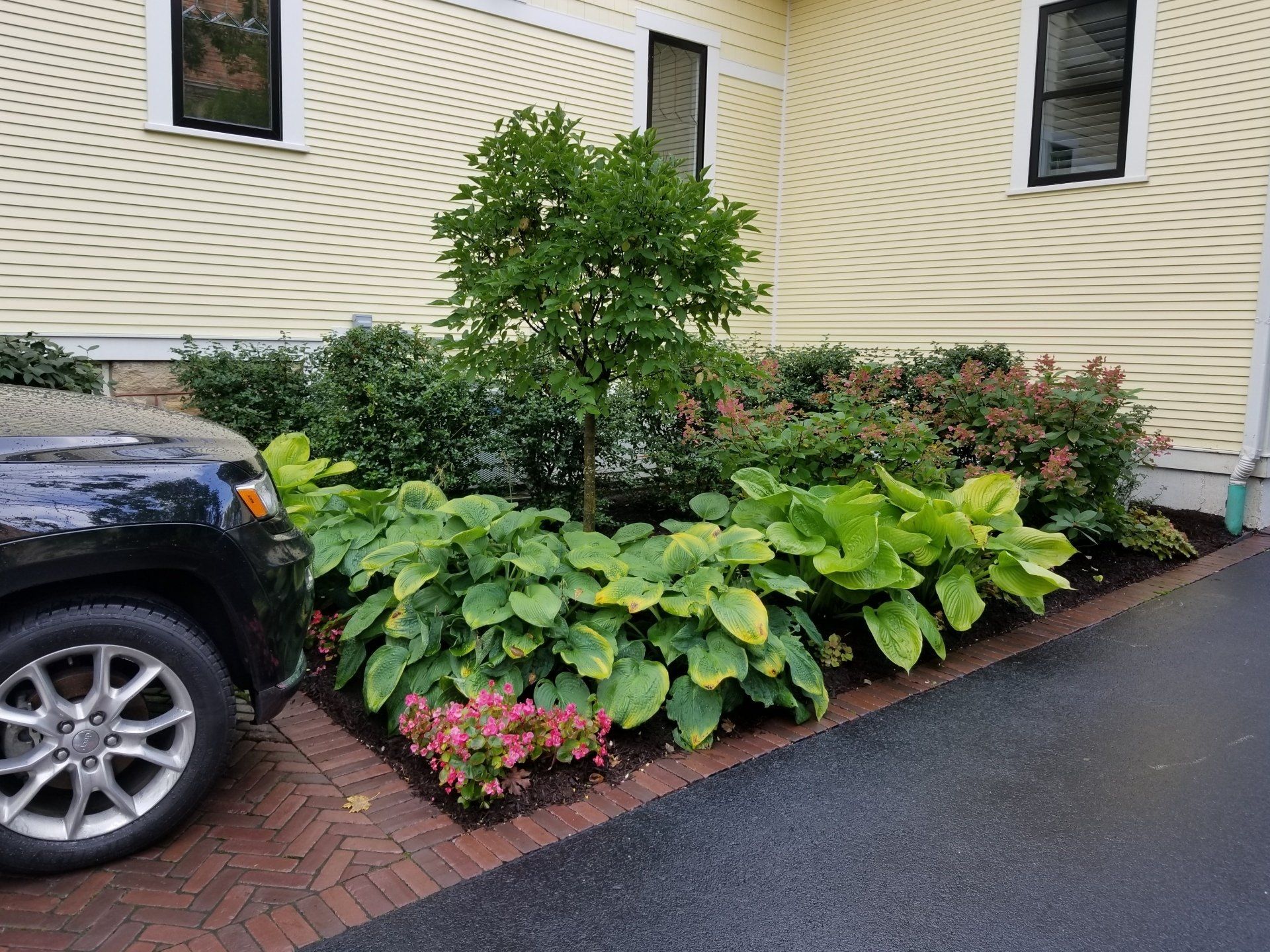 A black suv is parked in front of a yellow house.