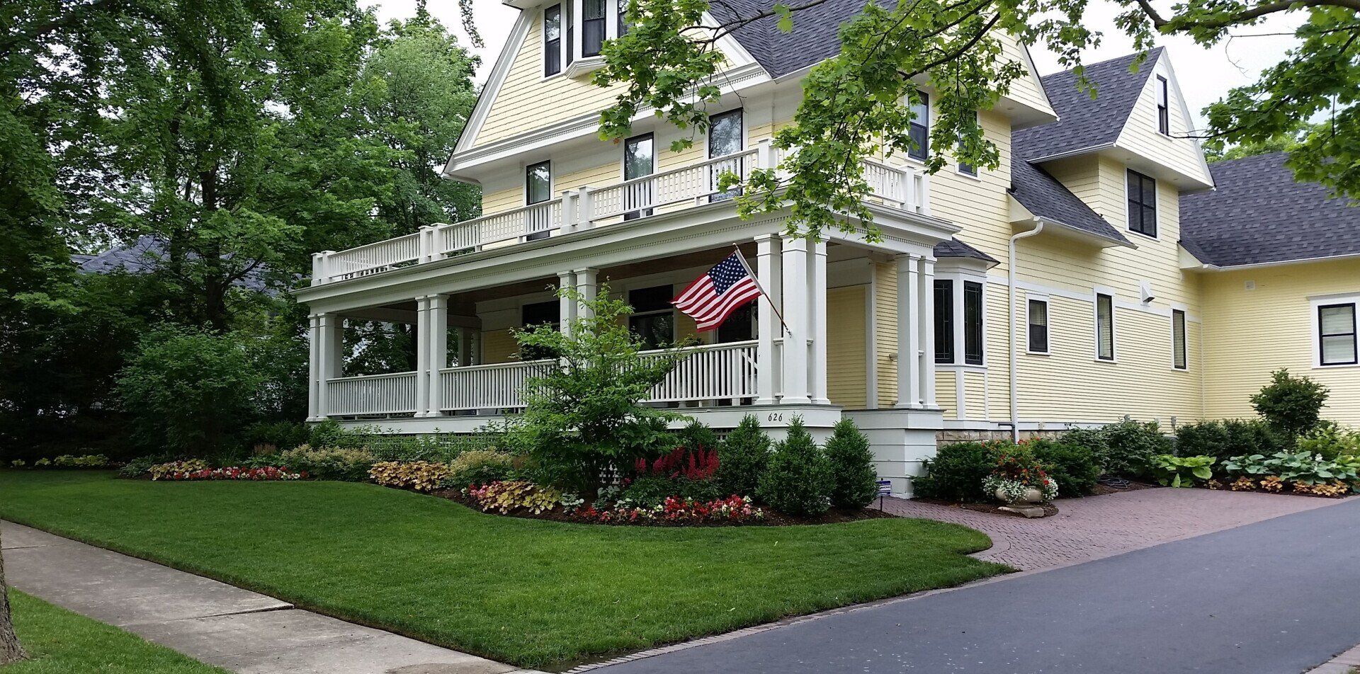 A large yellow house with a large porch and an american flag on it