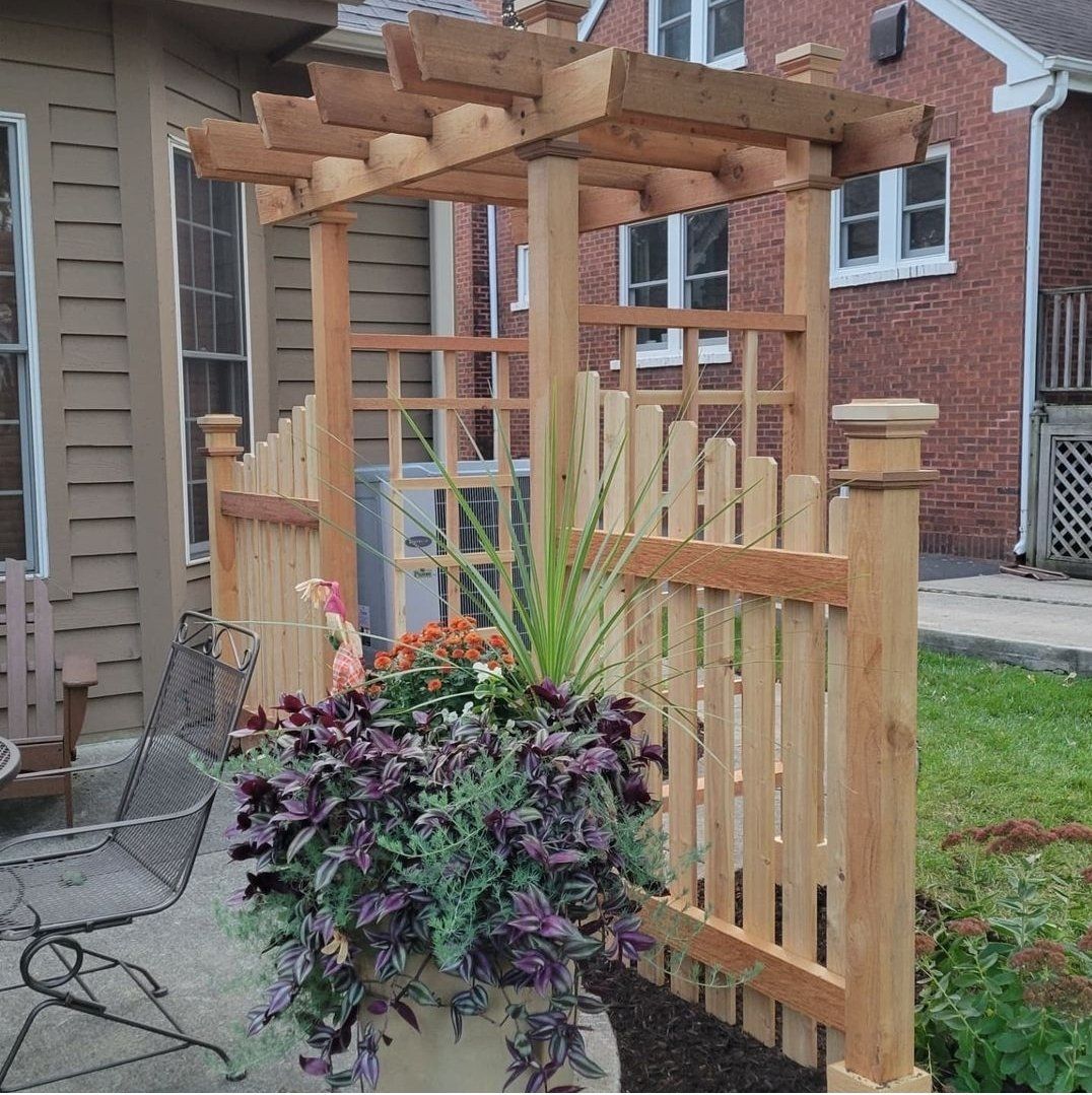 A wooden pergola with purple flowers in front of a brick house