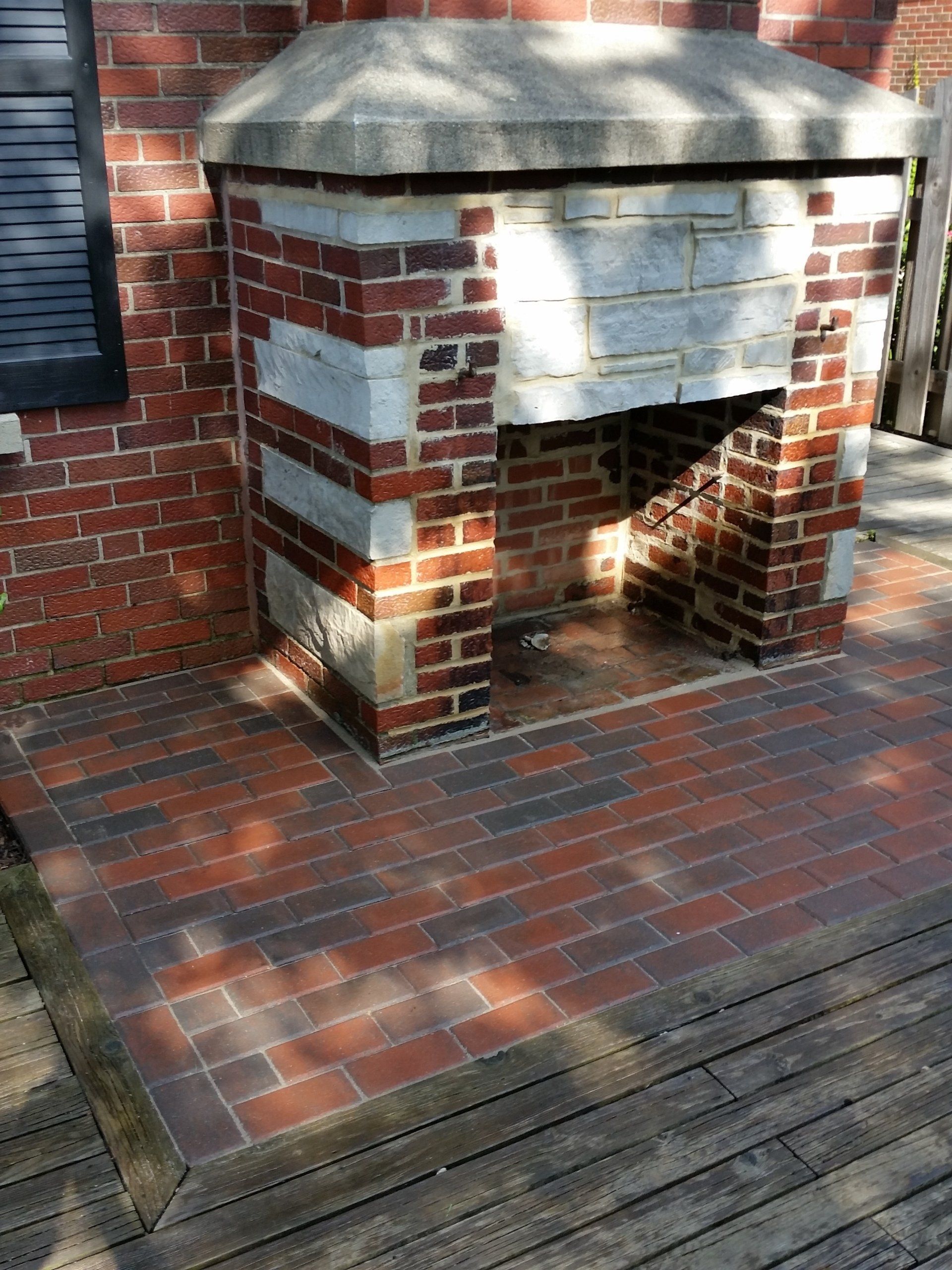 A brick fireplace is sitting on a wooden deck in front of a brick building.