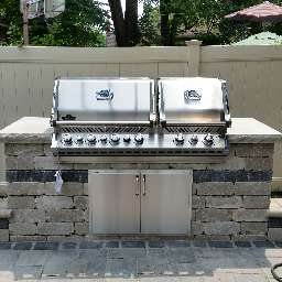 A stainless steel grill is sitting on top of a stone wall.