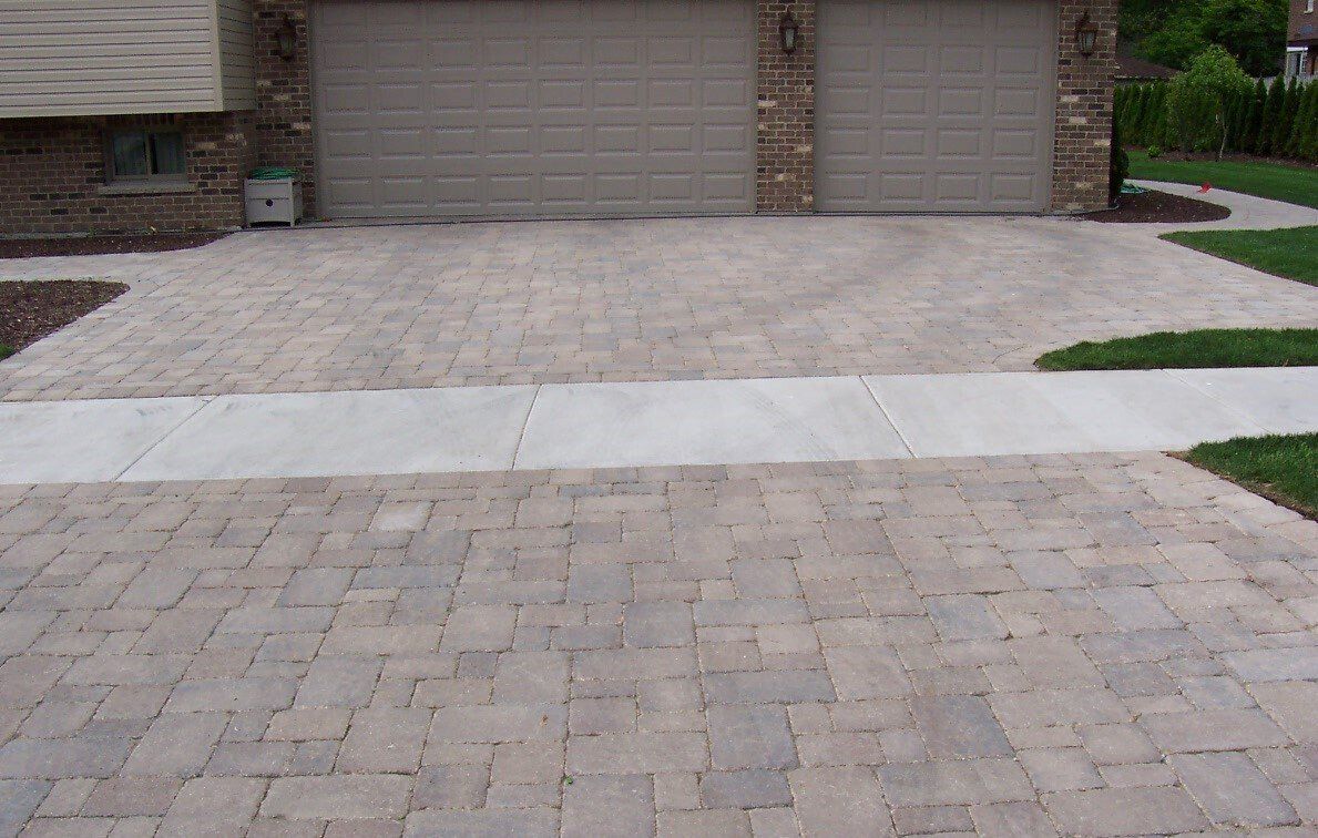 A driveway leading to a house with two garage doors and a sidewalk.