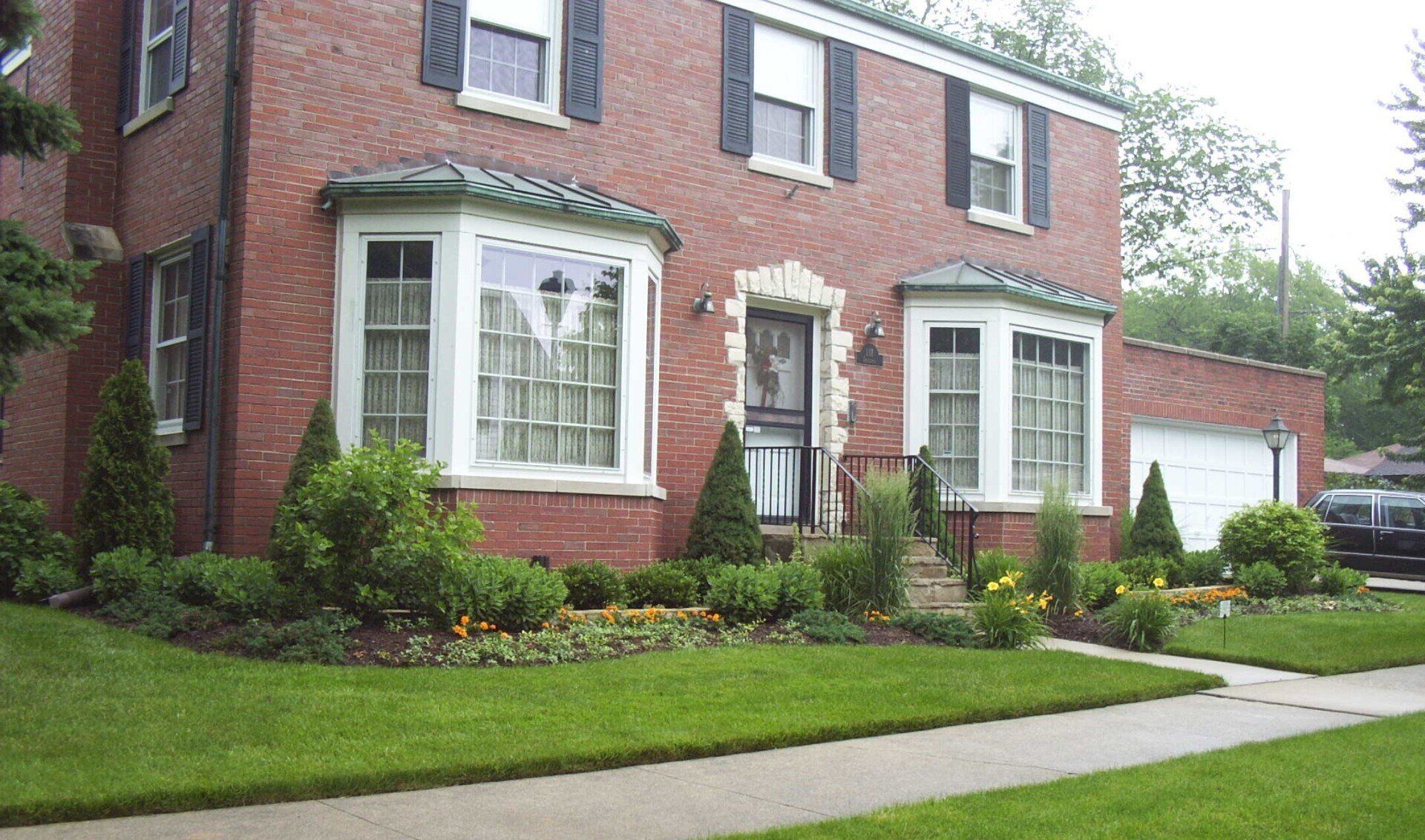 A brick house with black shutters and a lush green lawn