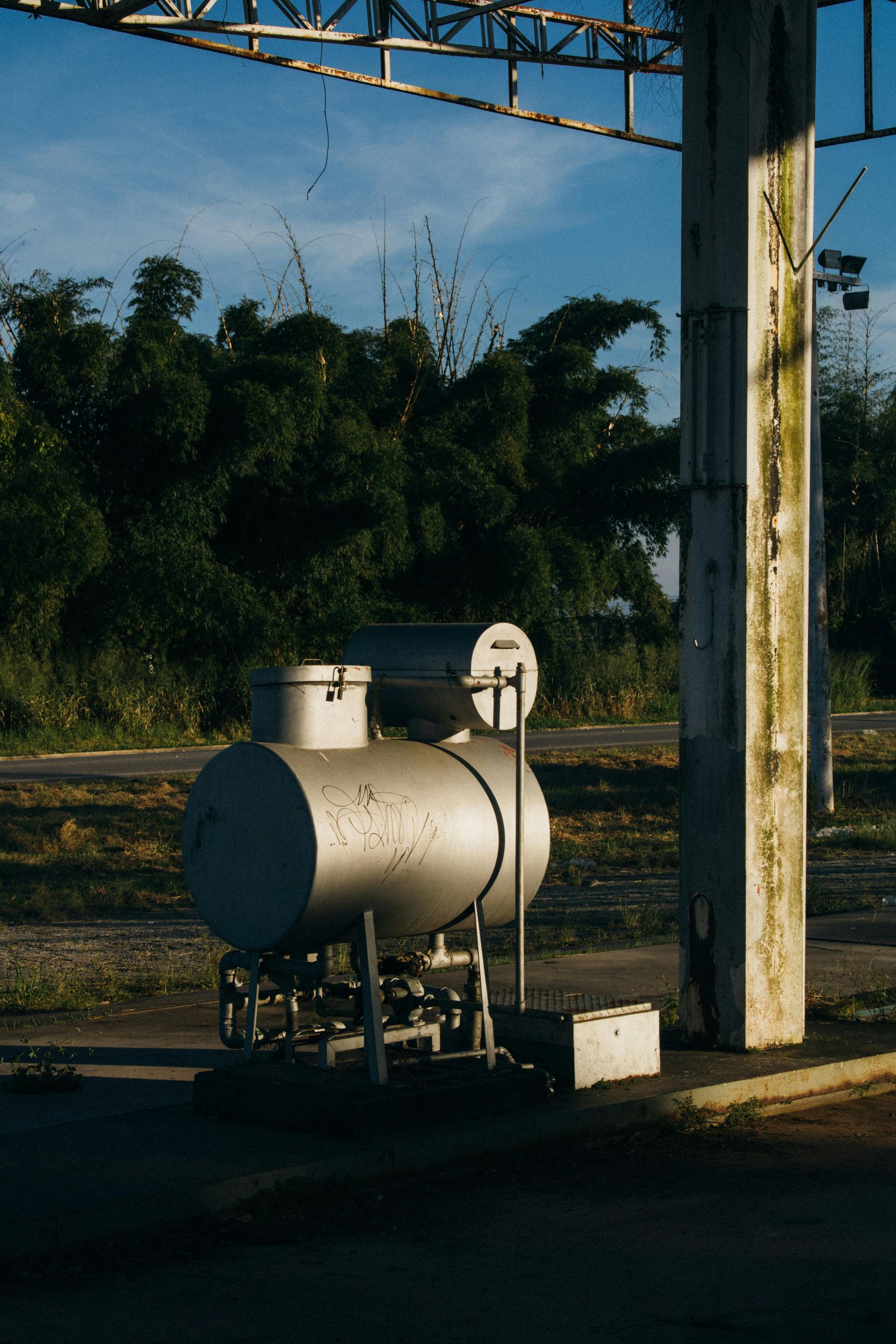 A large metal tank is sitting on the side of the road next to a pole.