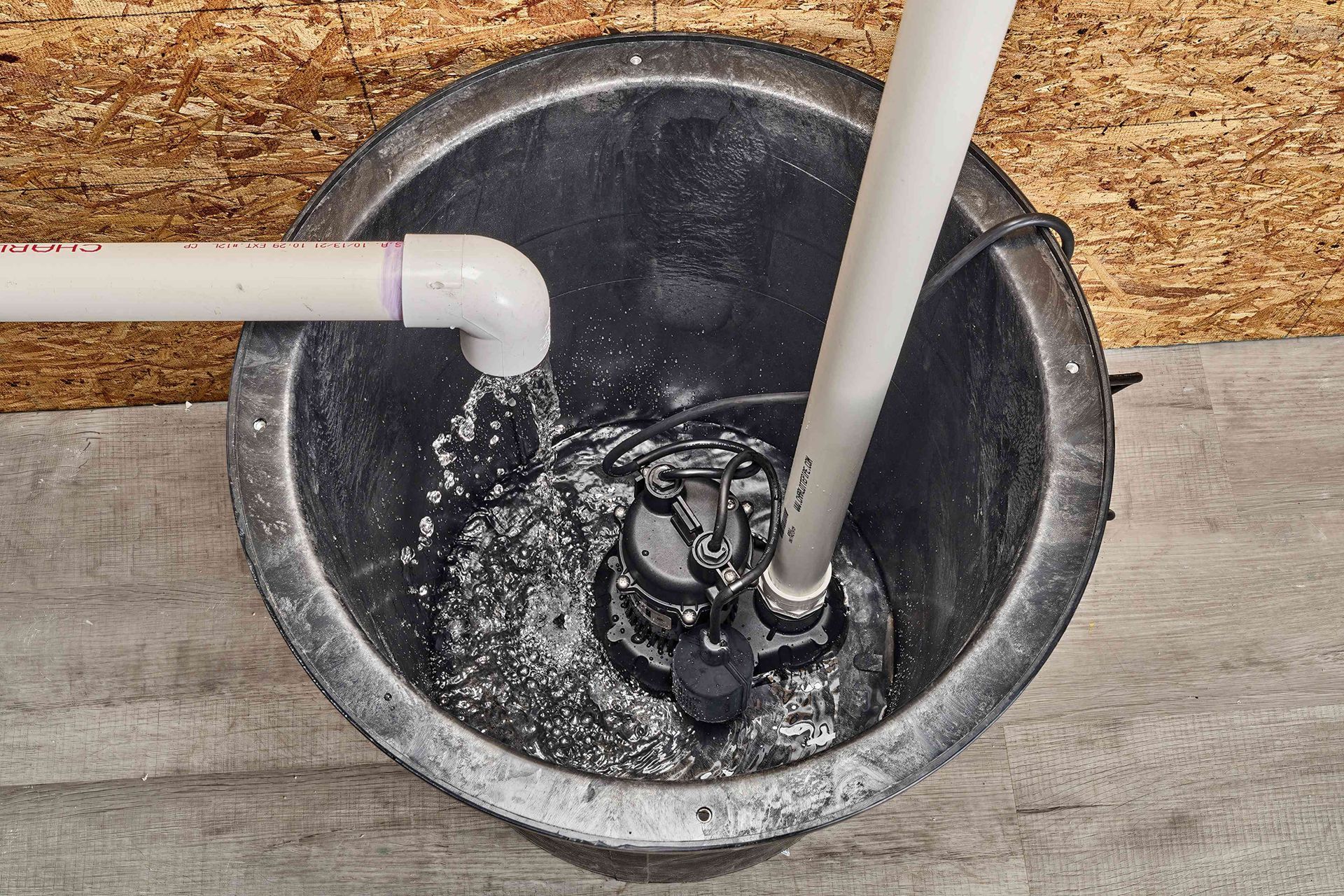 A sump pump system in a black basin with water, PVC pipes, and a pump.