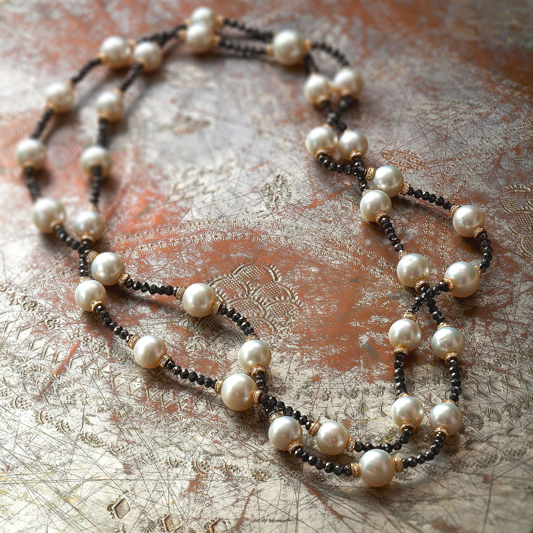 Pearl necklace with cream-colored beads and black beads on a textured, bronze surface.
