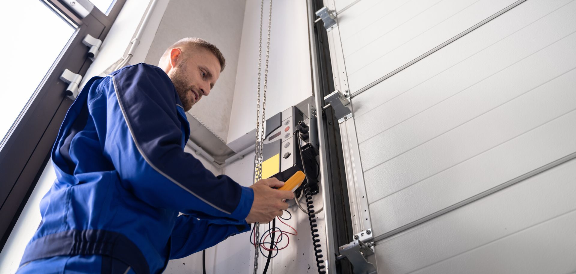 Technician testing a garage door opener control panel with a handheld meter indoors.