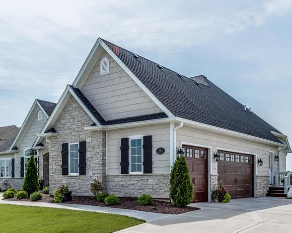 A large white house with a black roof and two garage doors.