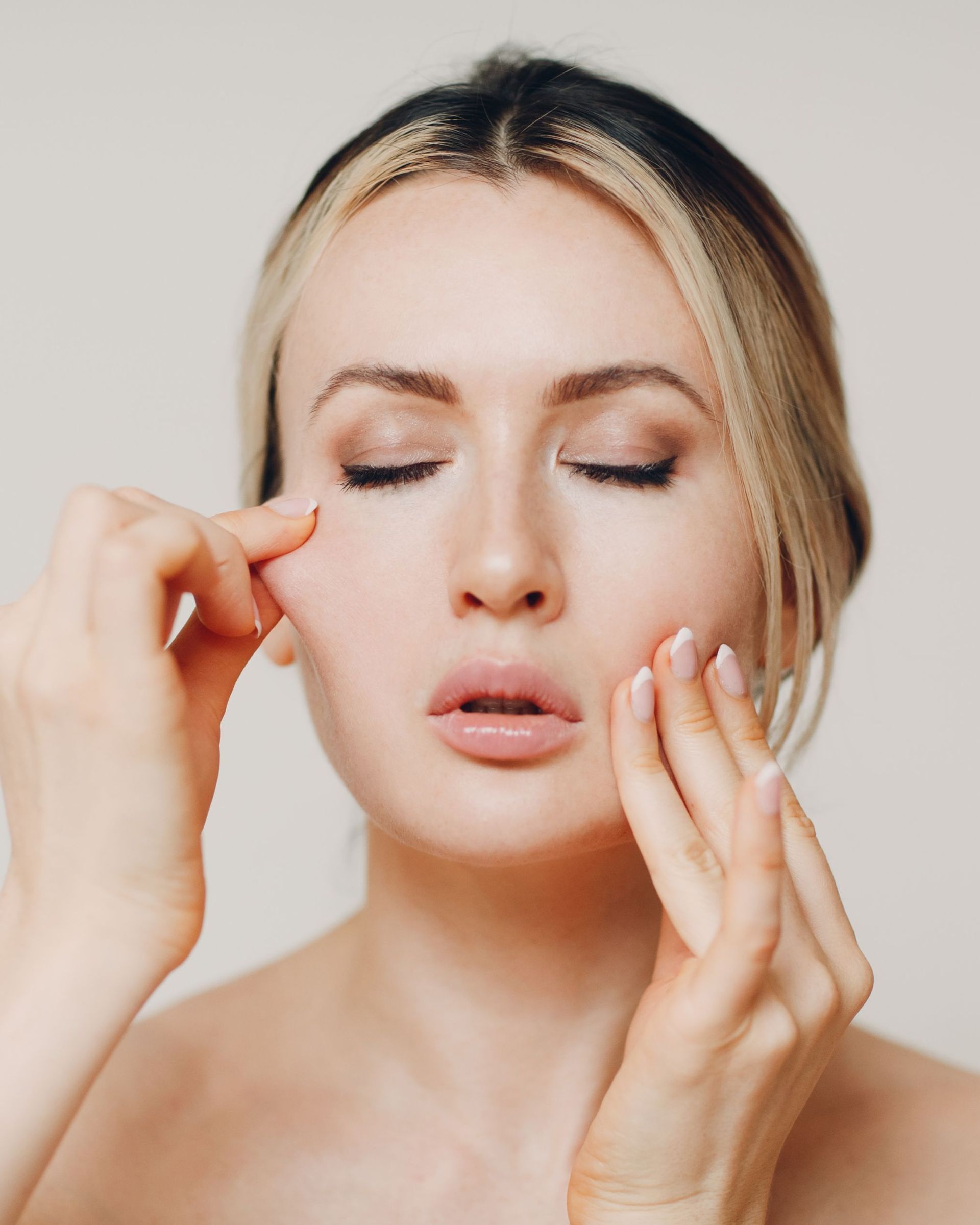 Woman with eyes closed, pulling skin on her face with her fingers.