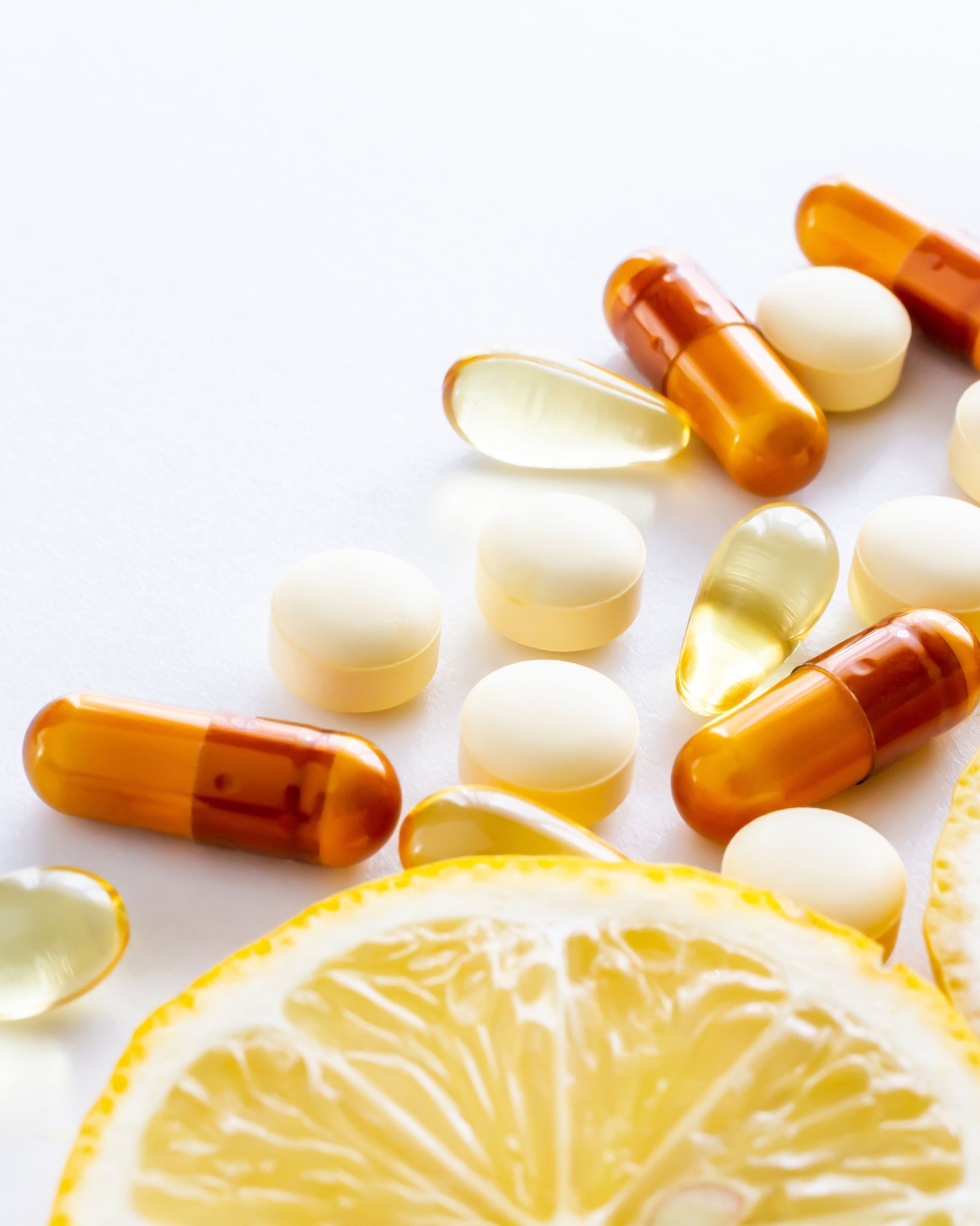 Pills and capsules alongside a slice of lemon on a white background.