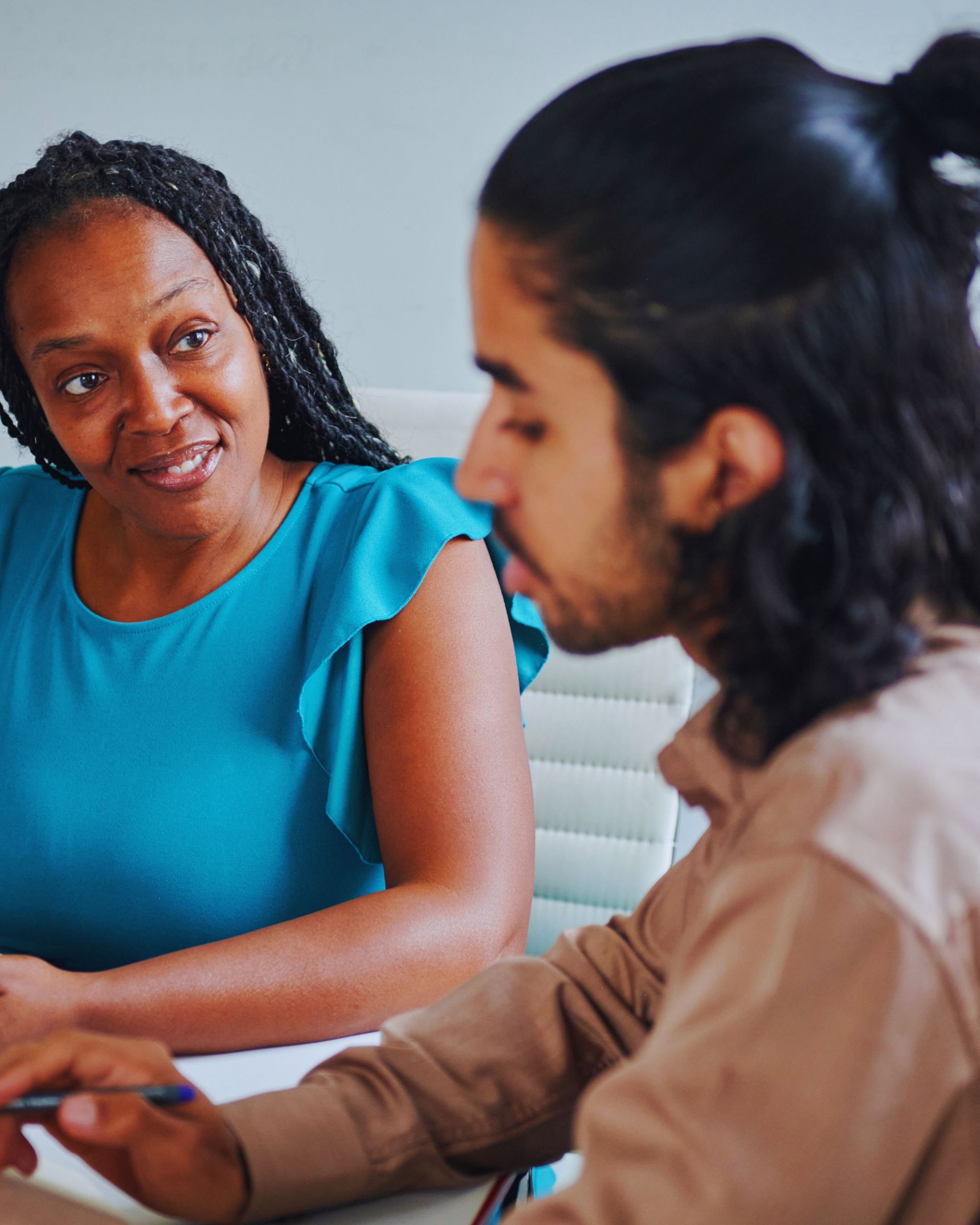 Woman in blue top looks at person with long hair, both indoors.