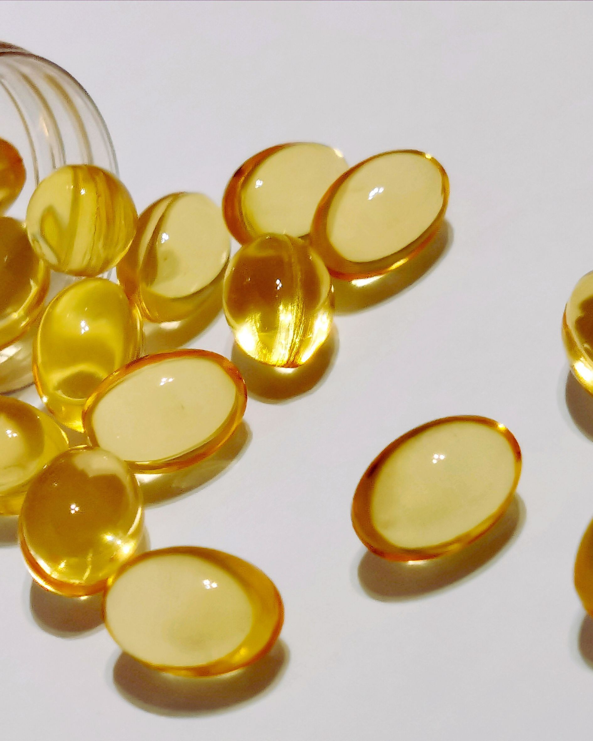 Yellow oval capsules spilling from a bottle on a white surface.