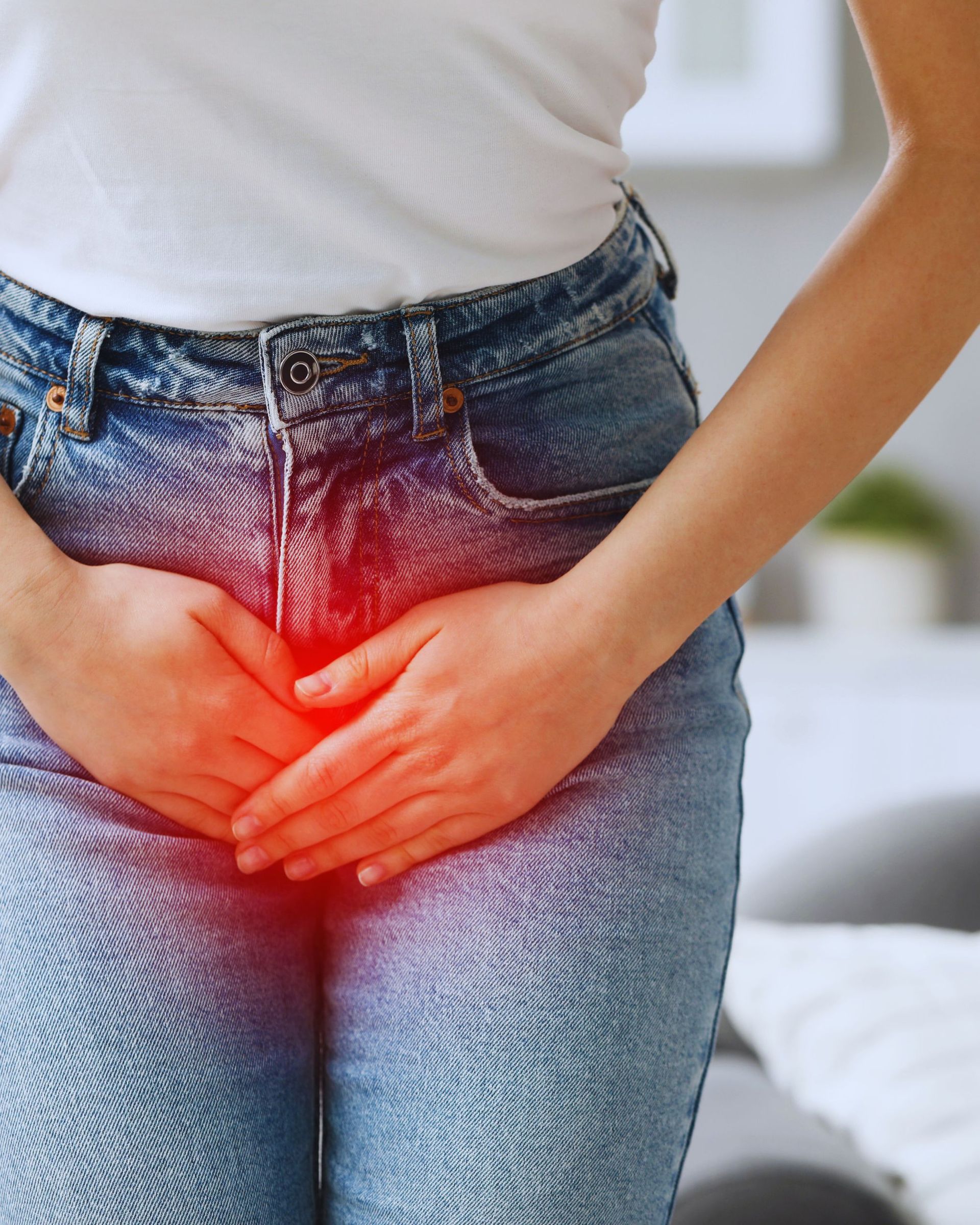 Person in jeans holds hands over pelvic area, indicating potential pain or discomfort. Red highlights pelvic region.
