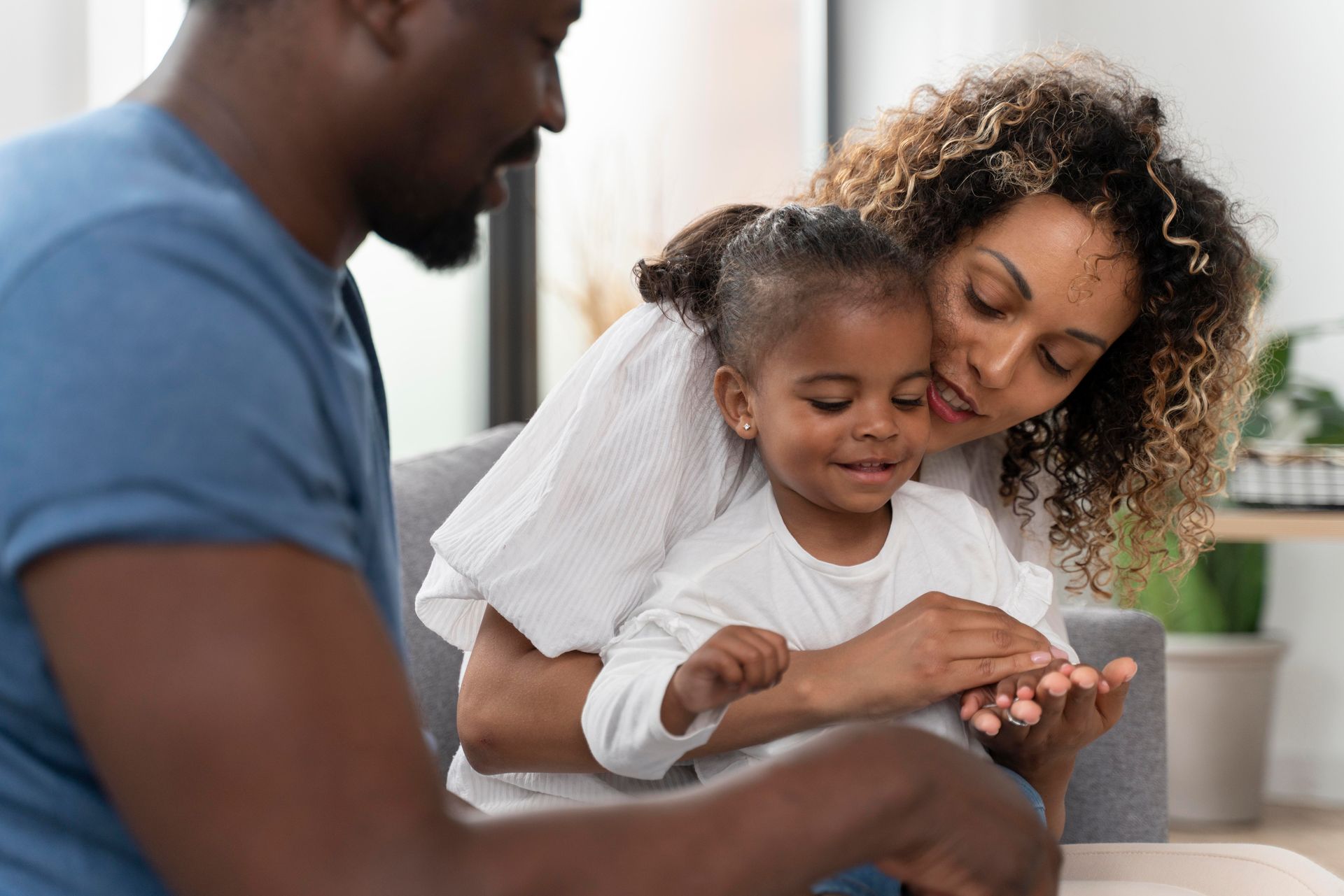 Man looking at a child on a woman's lap. The woman is smiling at the child.