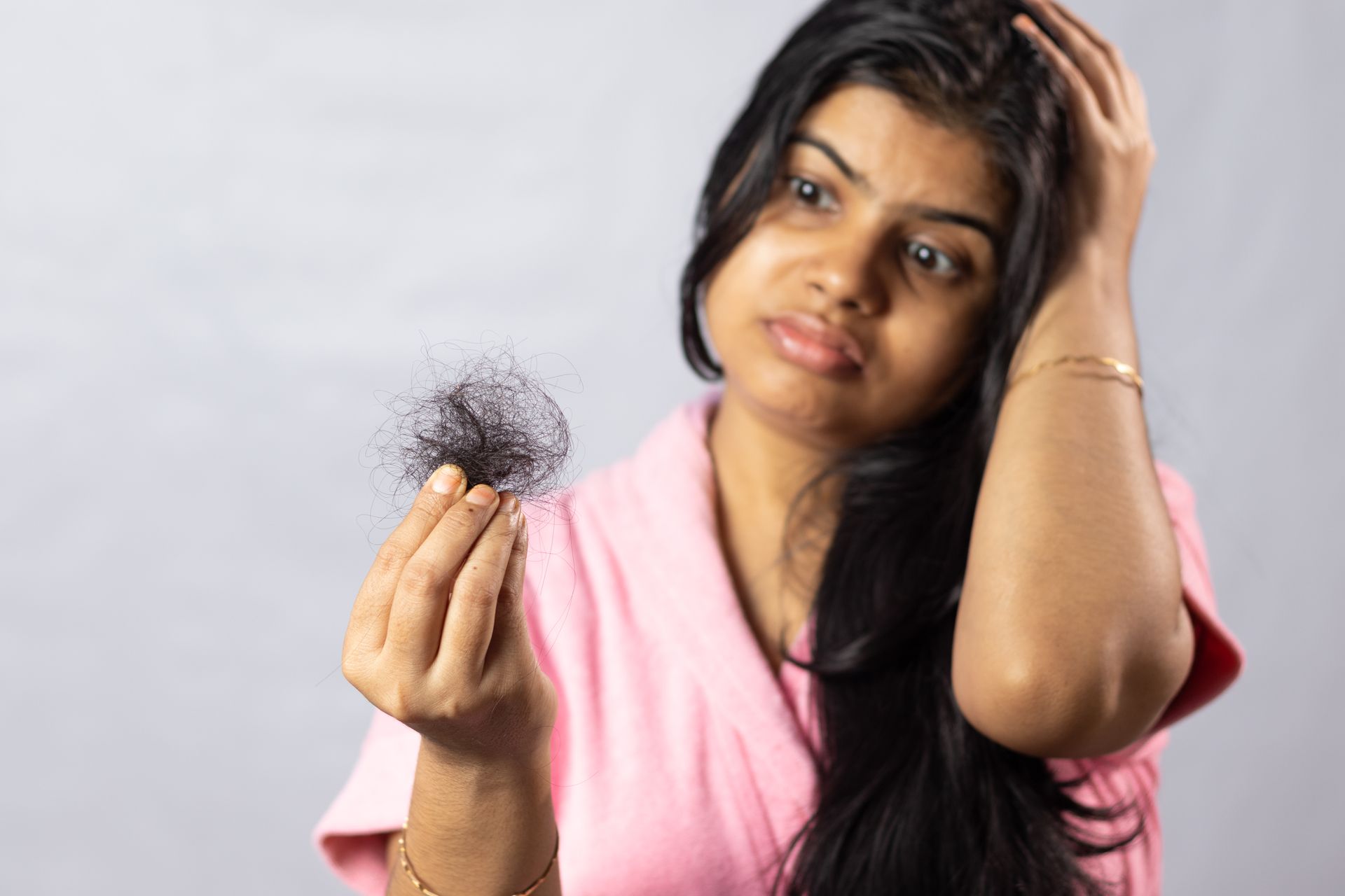 Woman looking at a clump of hair in her hand, concerned expression.