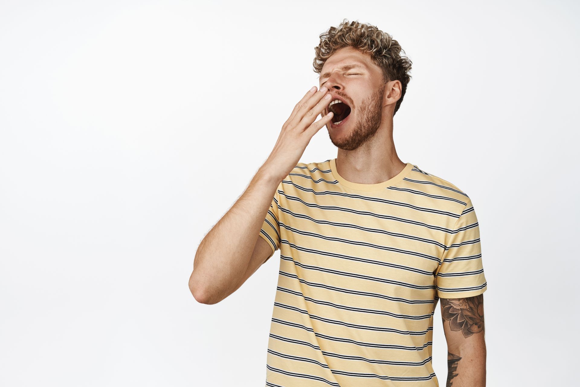 Man in striped shirt yawning, covering mouth with hand.