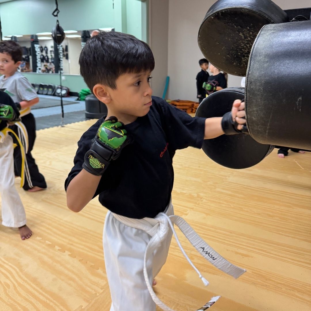 A young girl in a karate uniform is sitting on the floor.
