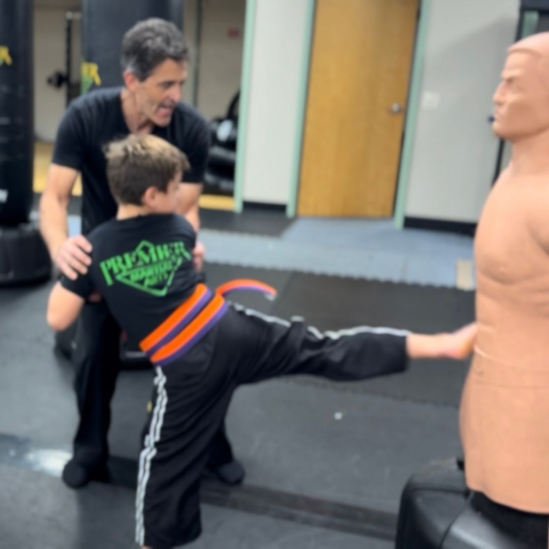A group of children are practicing karate with a teacher in a gym.