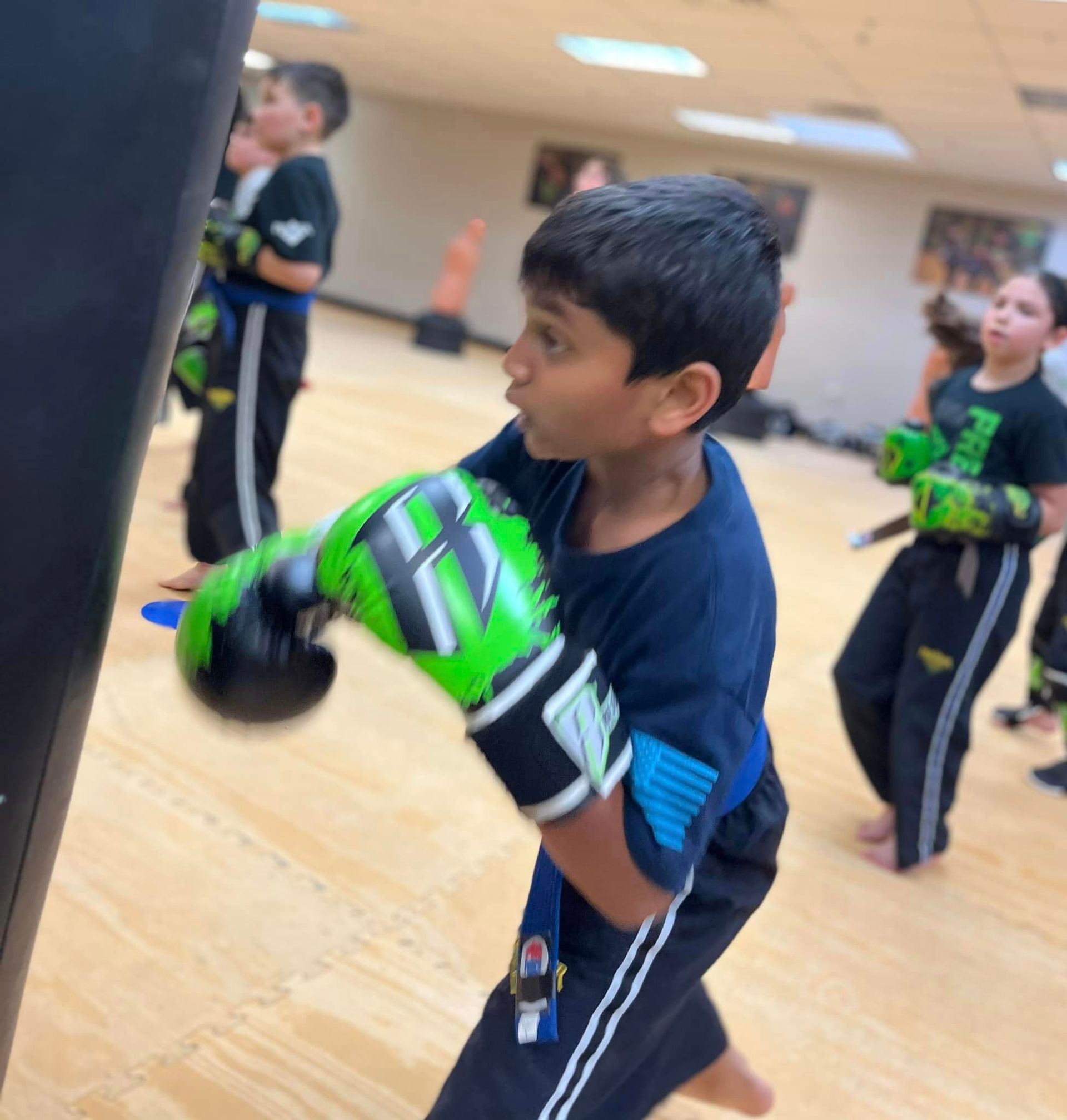 a little boy with boxing gloves punching a mat bag