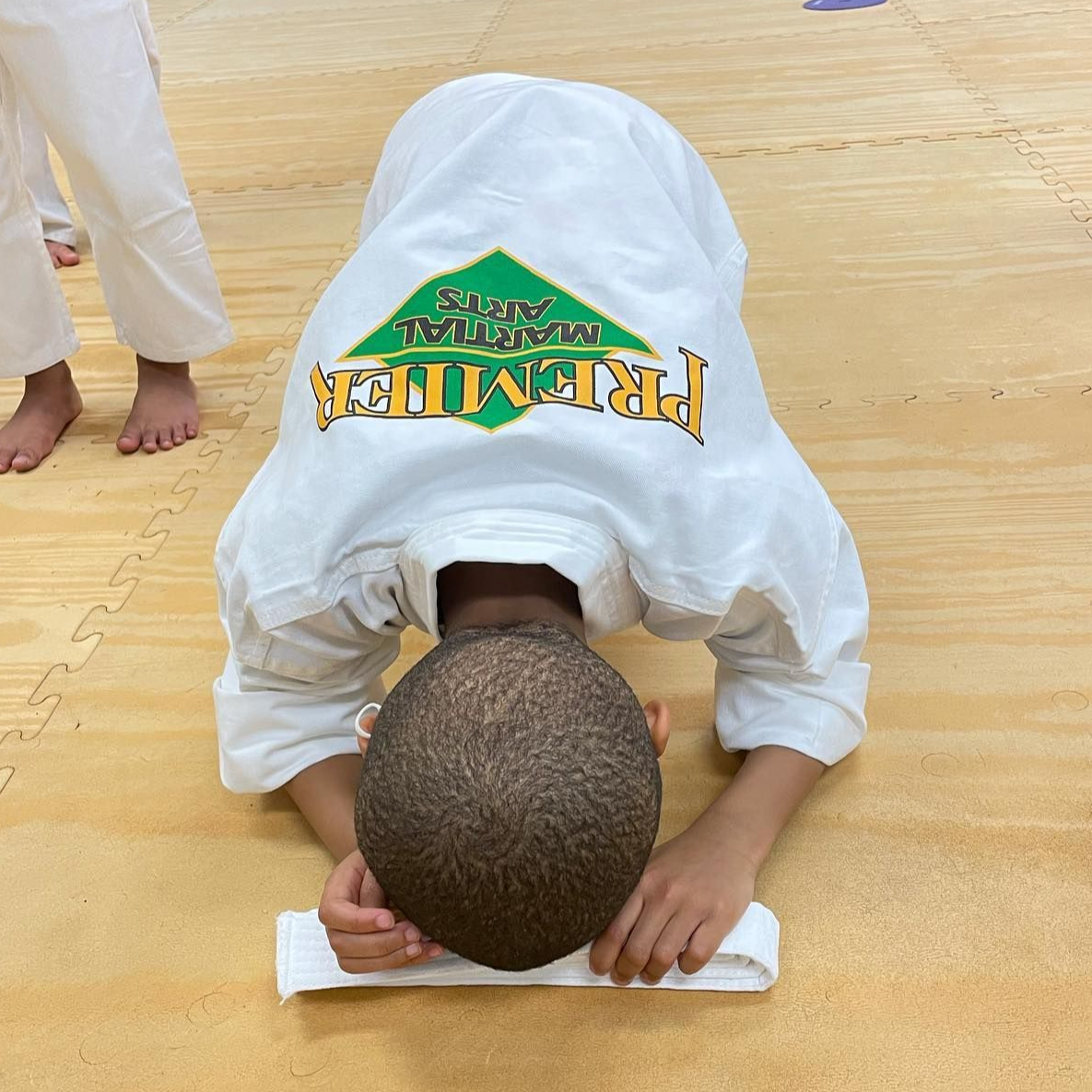A man is kneeling down next to a young boy in a taekwondo class.
