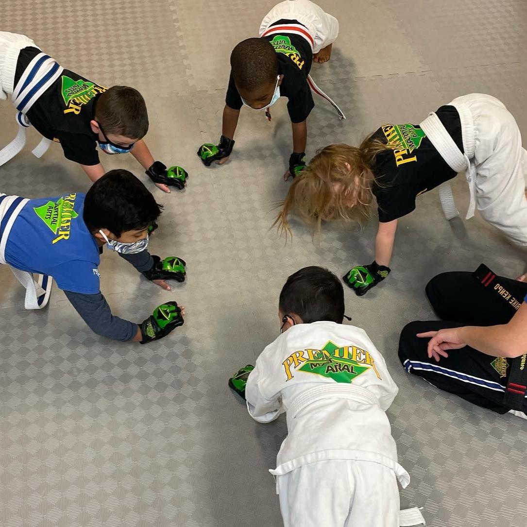 A young girl in a karate uniform is sitting on the floor.