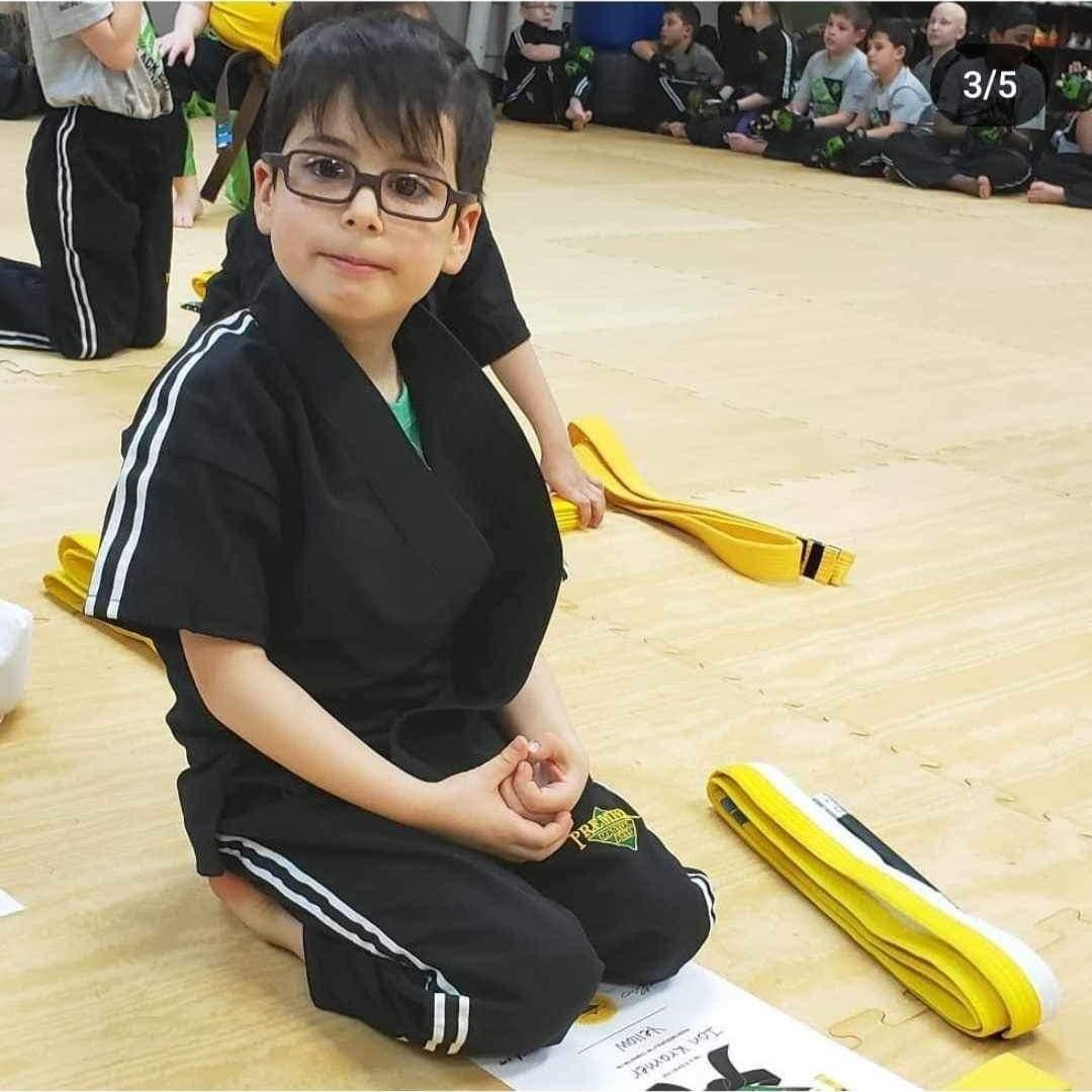 A man is kneeling down next to a young boy in a taekwondo class.