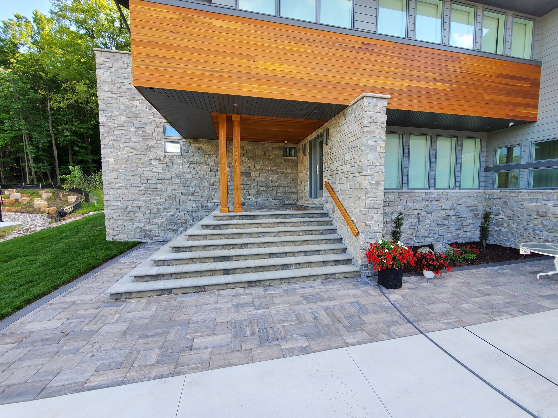 Modern house with stone facade, wooden accent above entrance, and paved steps leading to the door.