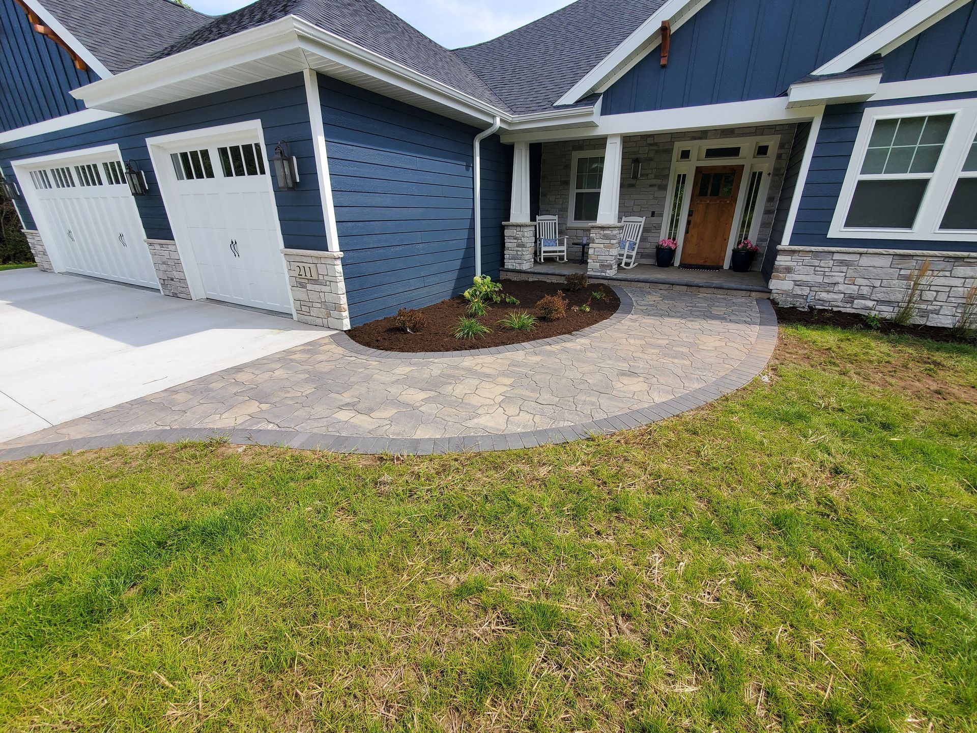 A blue house with a new brick walkway leading to the front door with some newly planted bushes and fresh mulch in Wausau, Wisconsin.