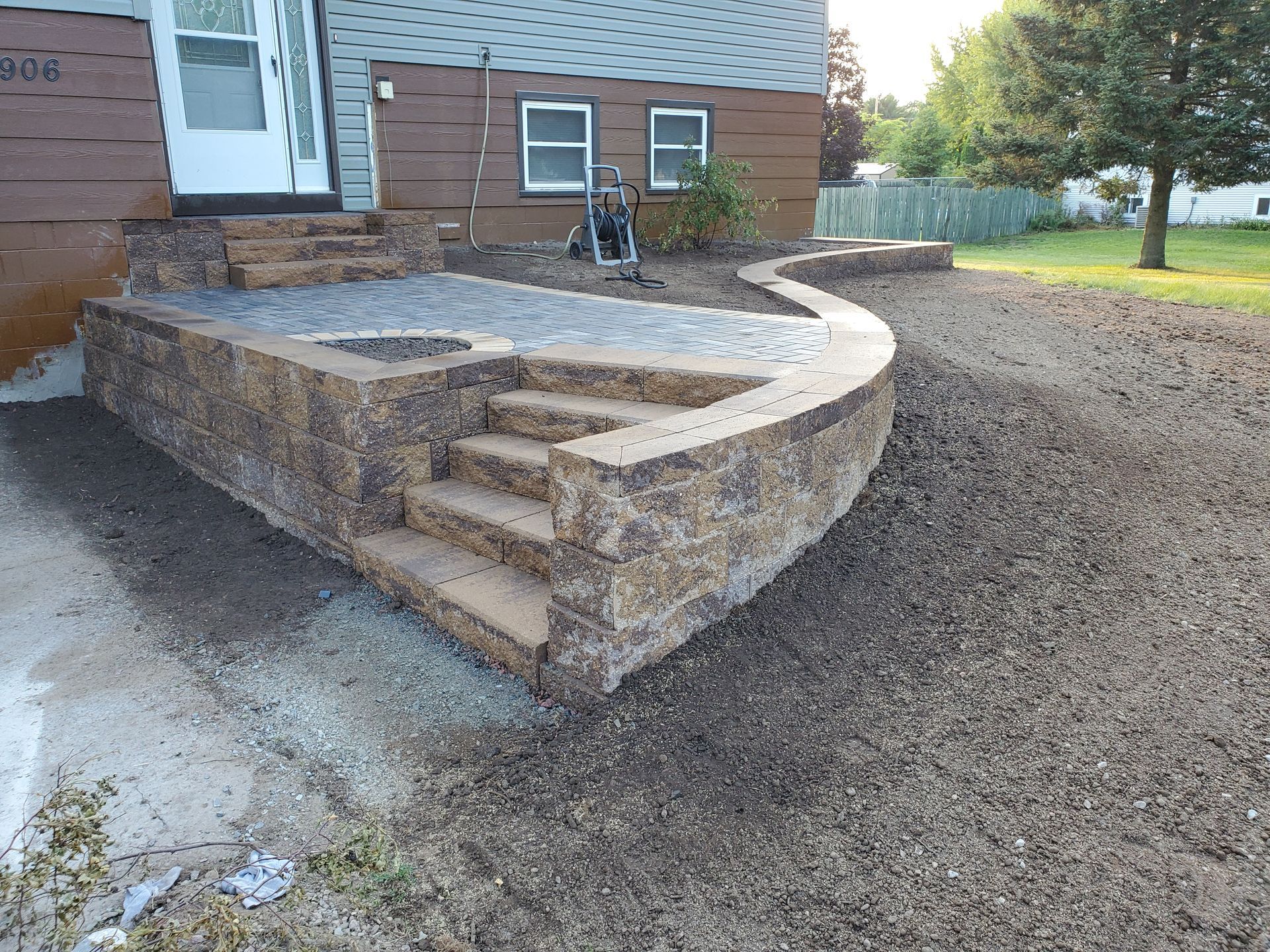 A stone wall with stairs and a fire pit in front of a house.