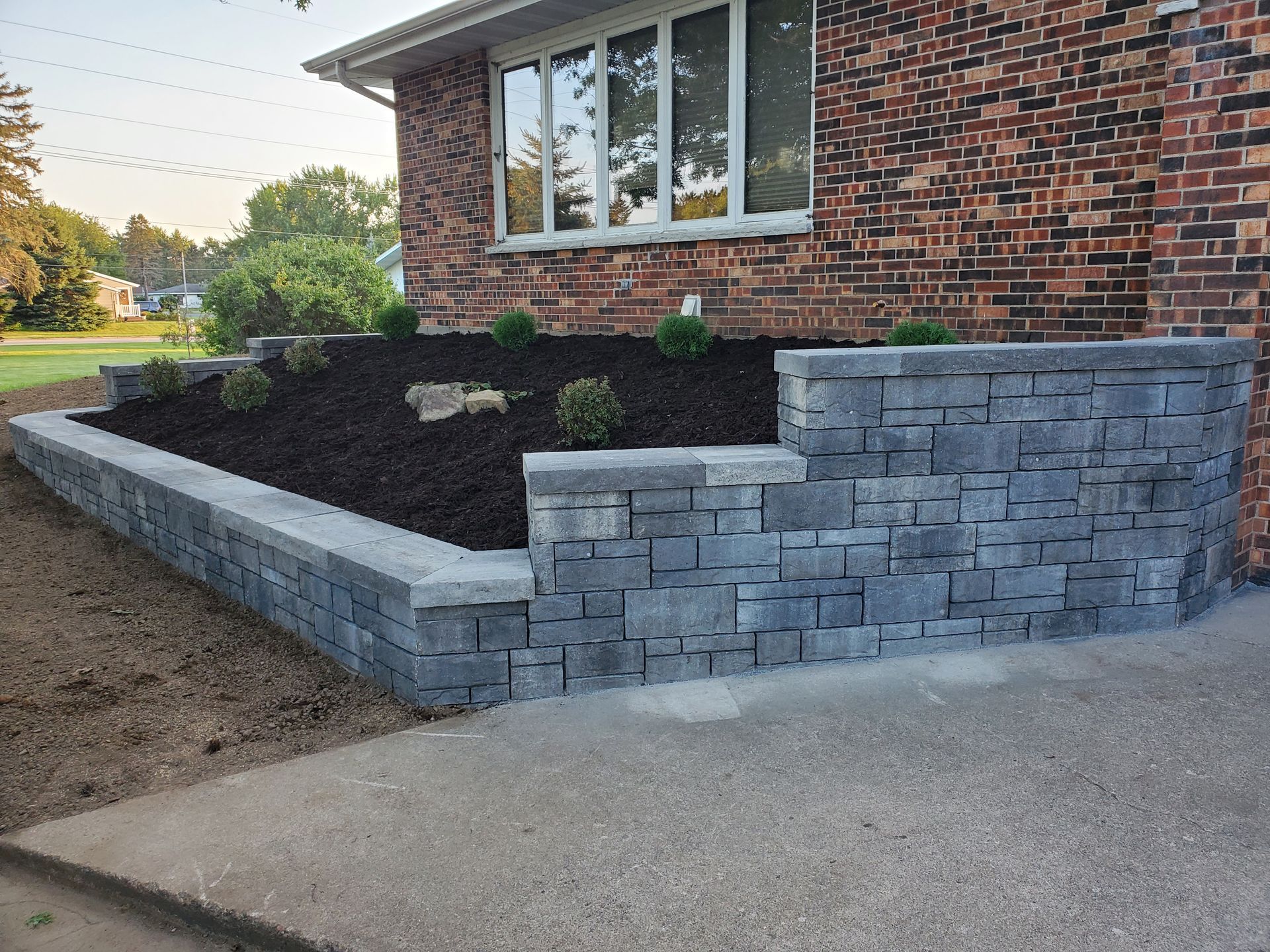Brick home with a gray stone retaining wall and landscaped flower bed.