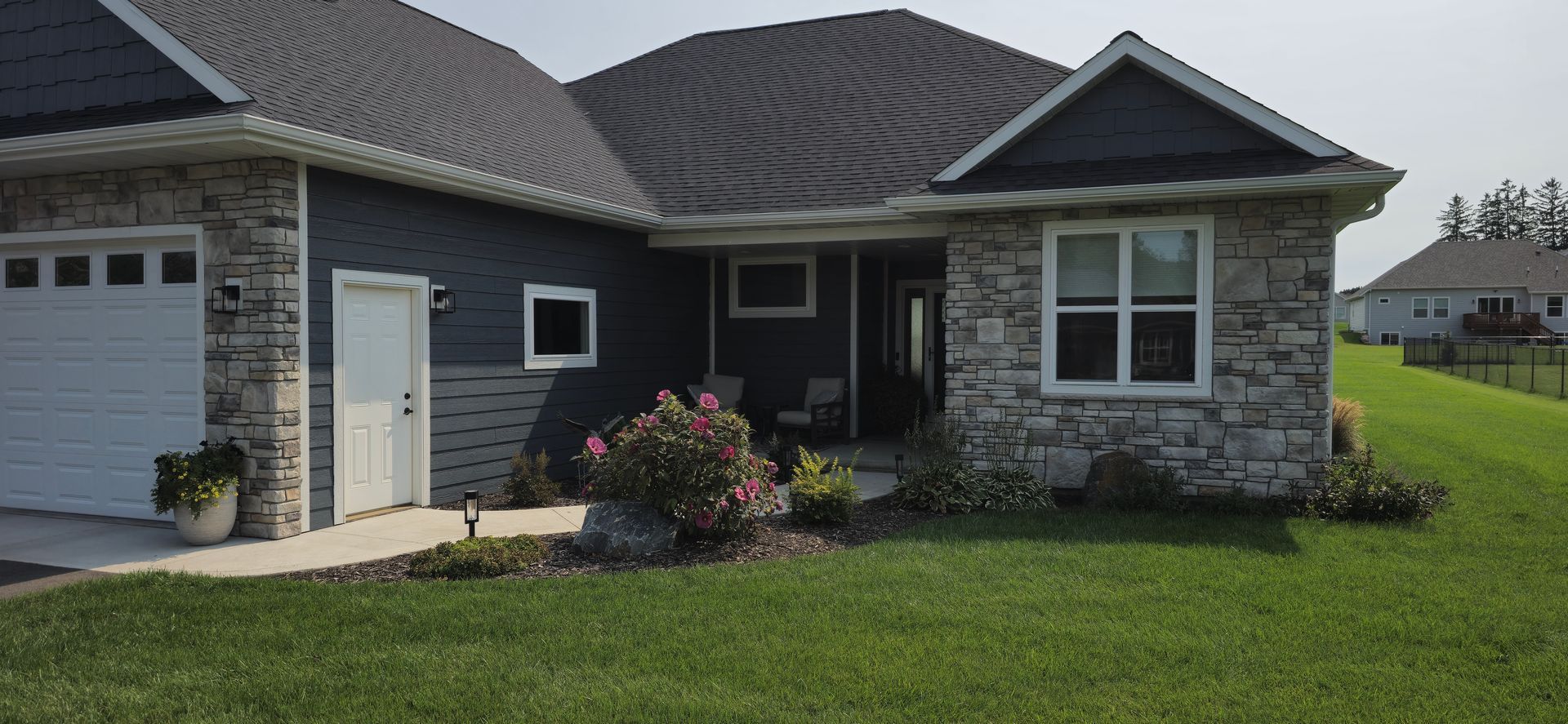 A house with a stone facade and a white garage door is sitting on top of a lush green lawn.