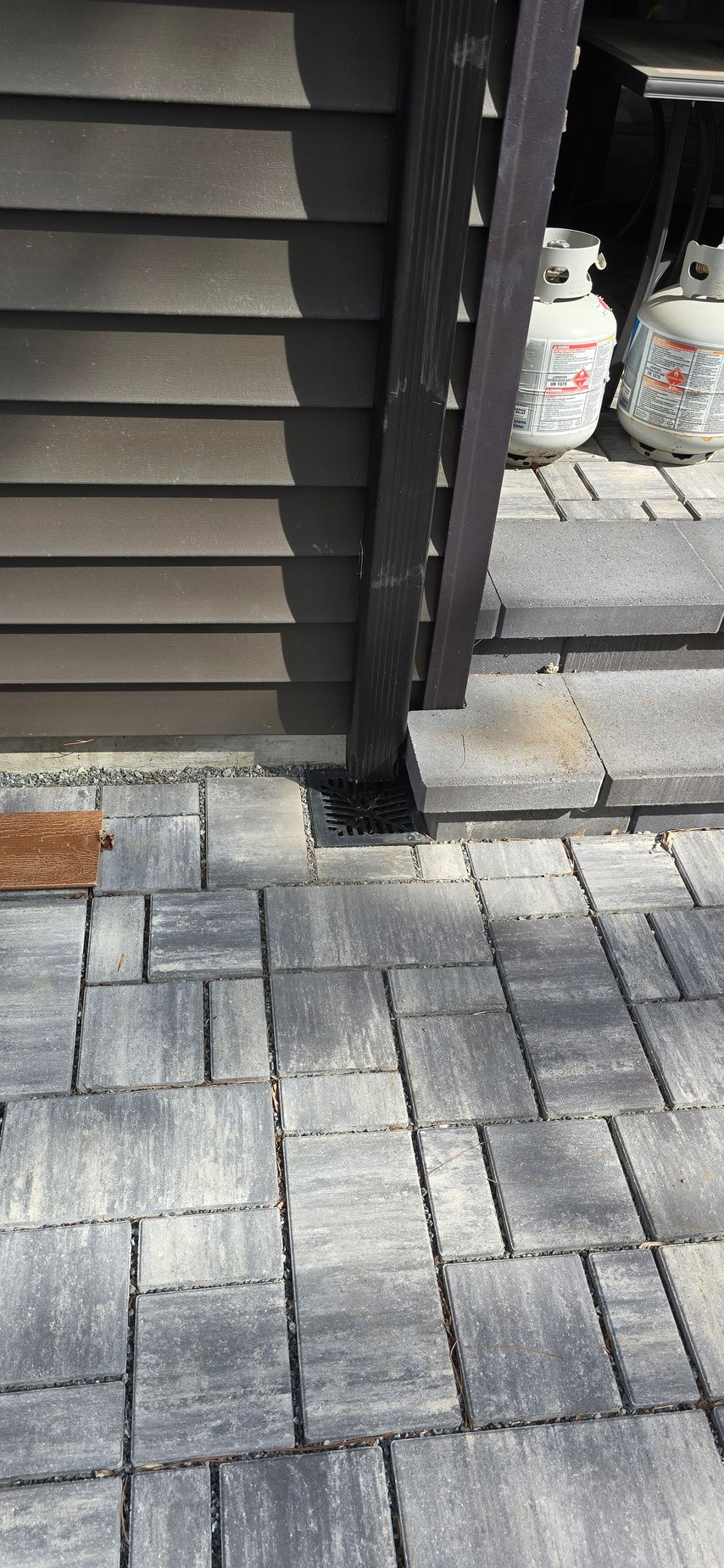 A brick walkway next to a house with propane tanks in the background.