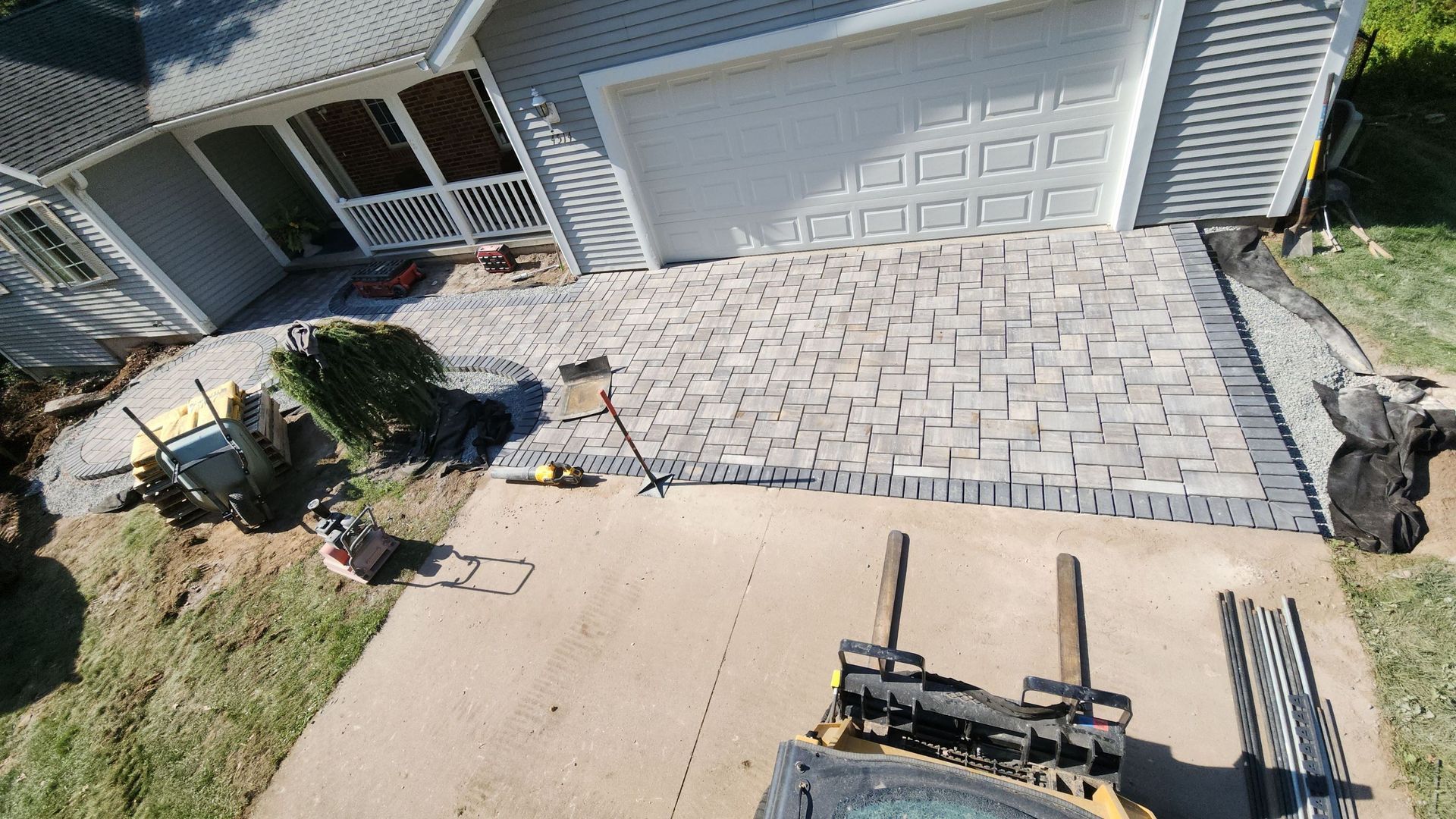 An aerial view of a brick driveway being built in front of a house.