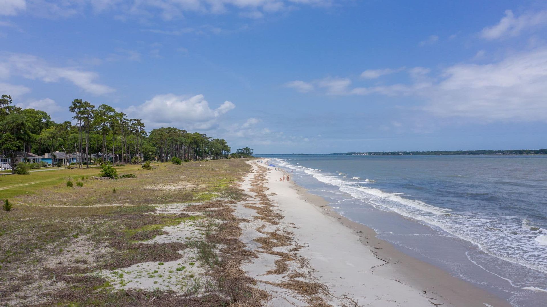 An aerial view of a sandy beach next to a body of water on a sunny day.